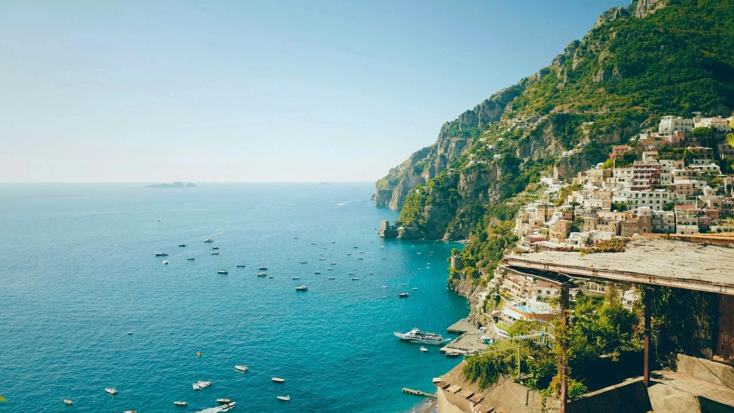 Cliffside colorful houses and luxury boats anchored in the turquoise waters of Positano along the Amalfi Coast, Italy.