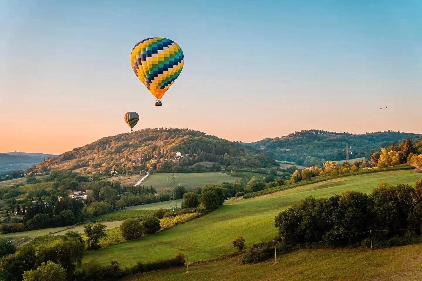 Hot air balloons floating above rolling green vineyards and hills in Tuscany at sunrise