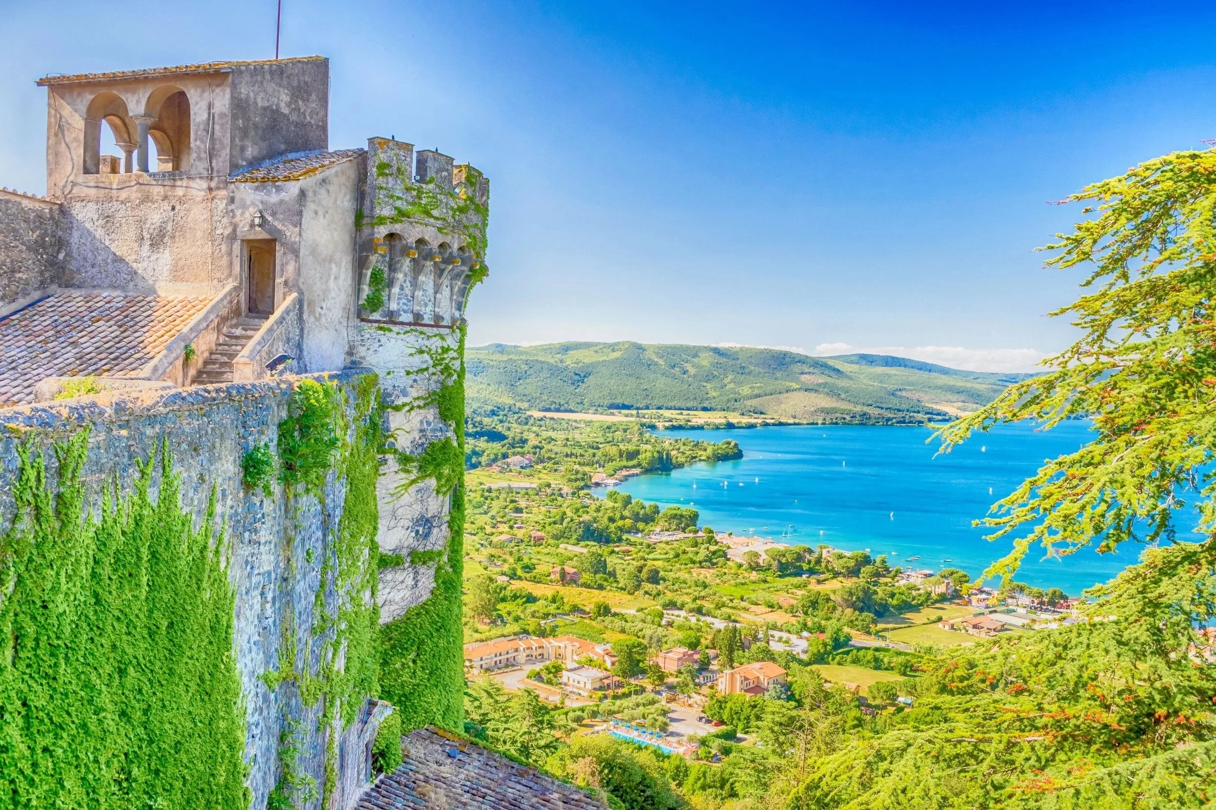 Ivy-covered medieval stone walls of Orsini-Odescalchi Castle overlooking the vibrant blue waters of Lake Bracciano in Lazio, Italy.