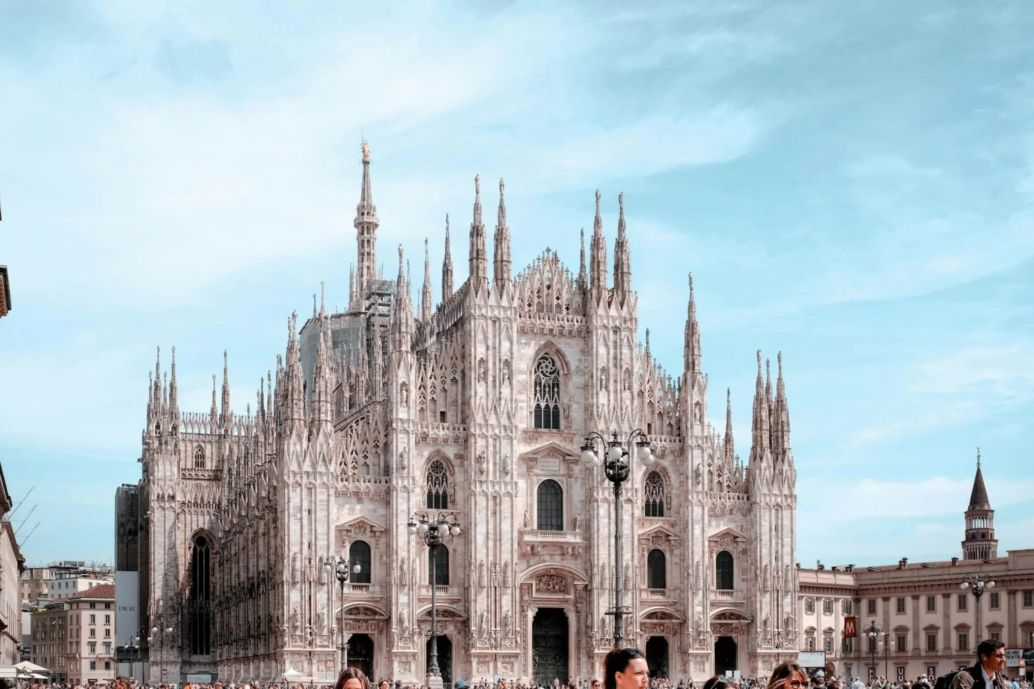 Exterior view of the marble facade and spires of the Duomo di Milano cathedral against a clear blue sky in Piazza del Duomo.