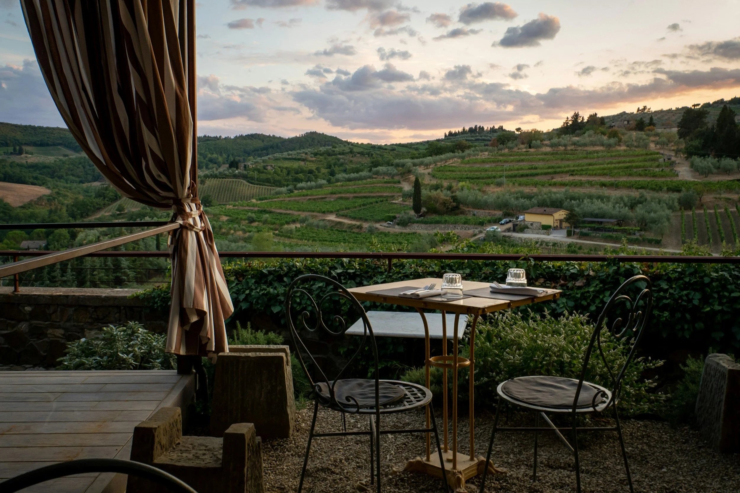 Outdoor dining table for two on a terrace overlooking rolling Tuscan vineyards and hills at sunset