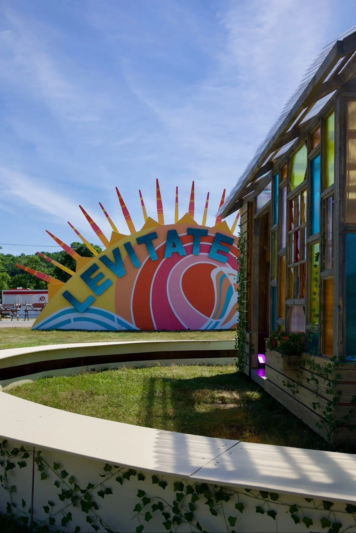 Colorful sign that reads 'LEEVITATE' with a sunburst design, next to a modern building with colorful windows and wooden siding, under a partly cloudy sky.