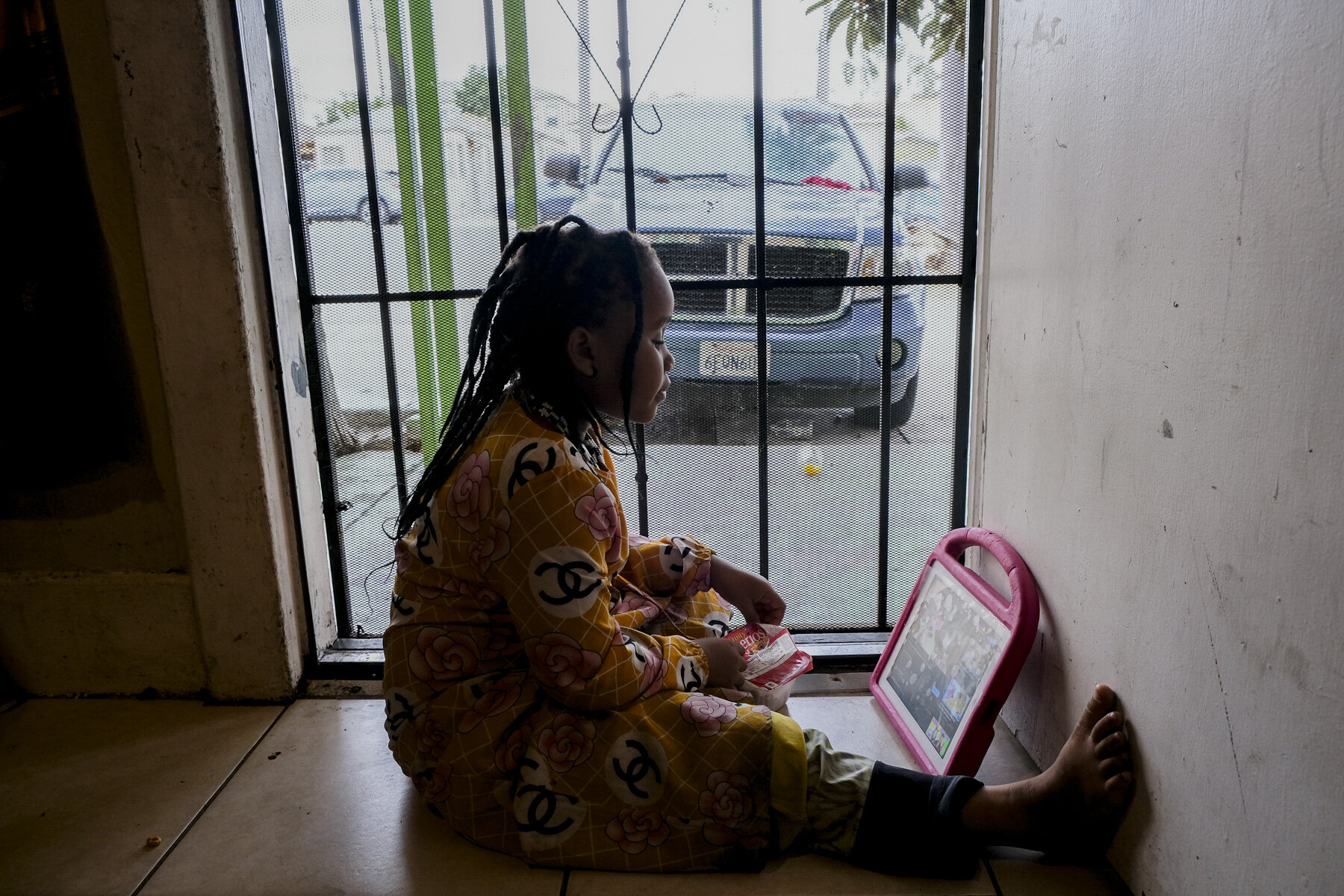  USA, San Diego, CA, November 5, 2020. After class, Musa’s niece, Nuriya, 7, changes her surroundings by sitting beside the door and watching YouTube. Nuriya has eight siblings and Musa watches most of them while her mother is at work. Photo ©Aryana 