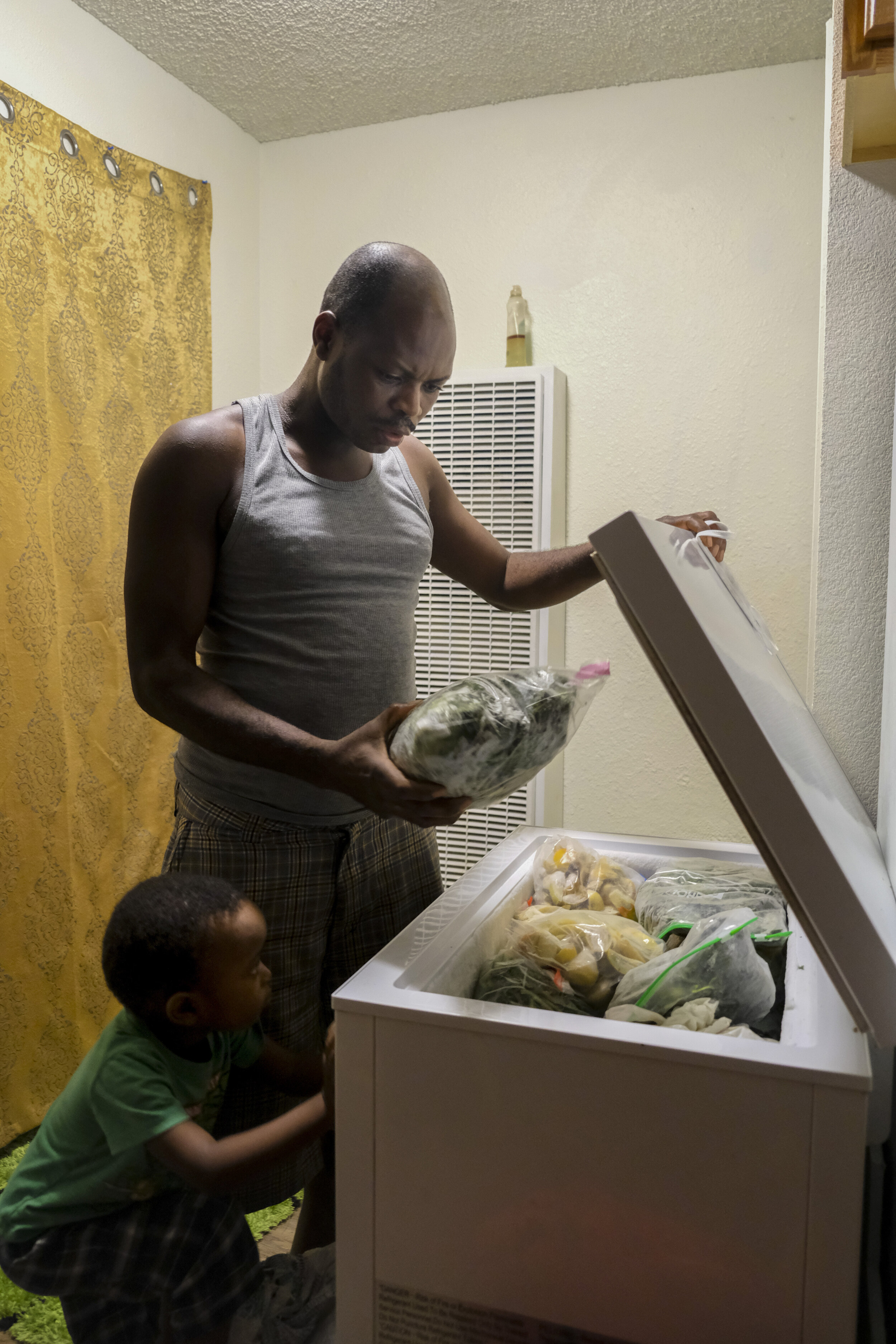  USA, San Diego, CA, October 27, 2020. Denis Sindayigaya, 3, watches his father Desire Ndayisenga, 40, select ingredients for dinner from the family’s storage freezer.&nbsp; After spending the day preparing food as a chef at BJ's Brewhouse, a restaur