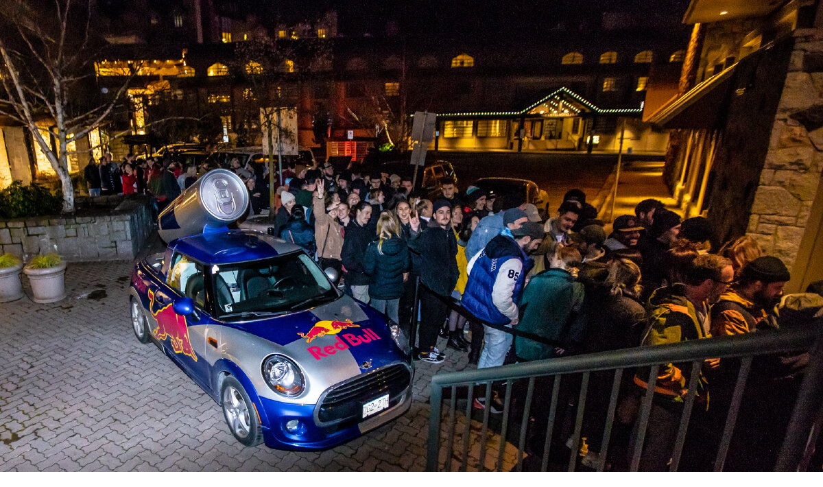 Massive lineup of people to enter Red Bull brand activation. Red Bull branded Cooper Mini parked out front.
