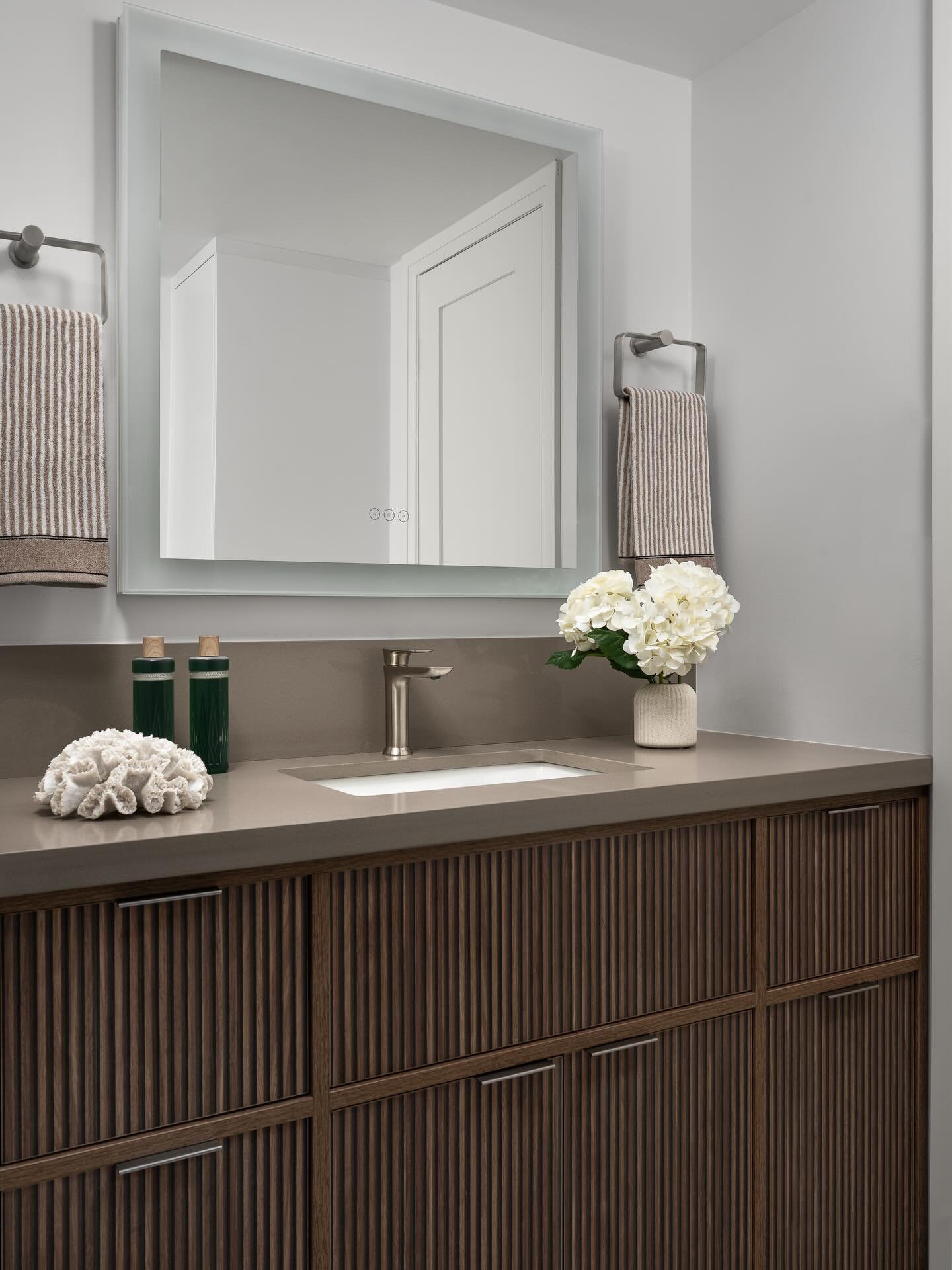 A bathroom designed for everyday ease!
By rethinking the layout, we created additional storage, expanded the counter space, and introduced reeded cabinetry for subtle texture. A softly lit LED mirror adds both function and atmosphere.

Photography by