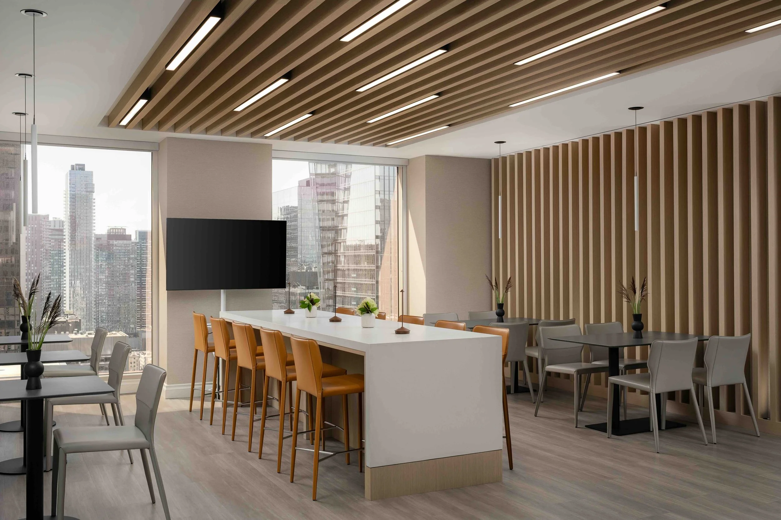 Modern office breakroom and lounge with communal island seating, wood slat ceiling, and panoramic city views in Toronto.