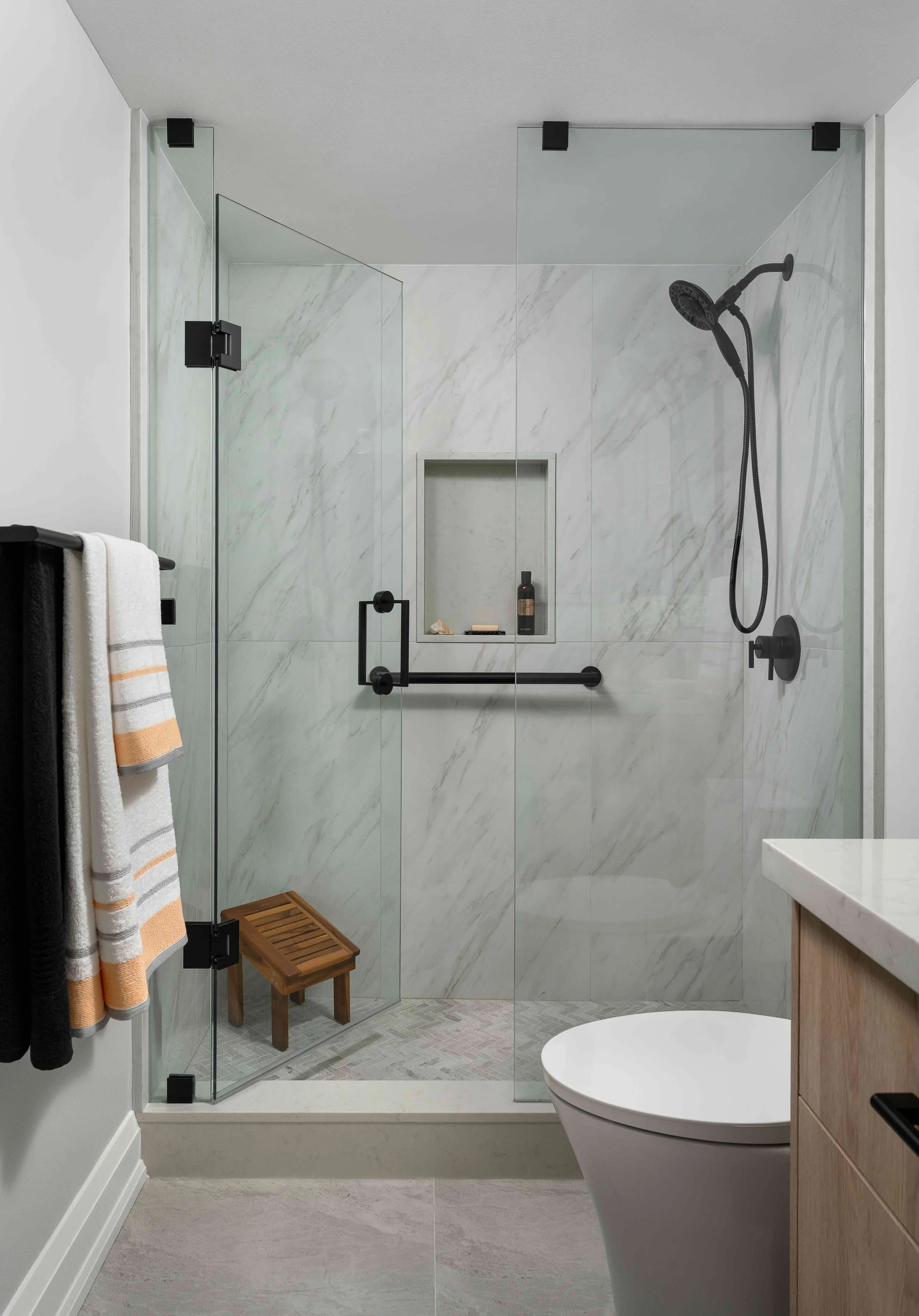 Modern condo bathroom with frameless glass shower and marble tile surround.
