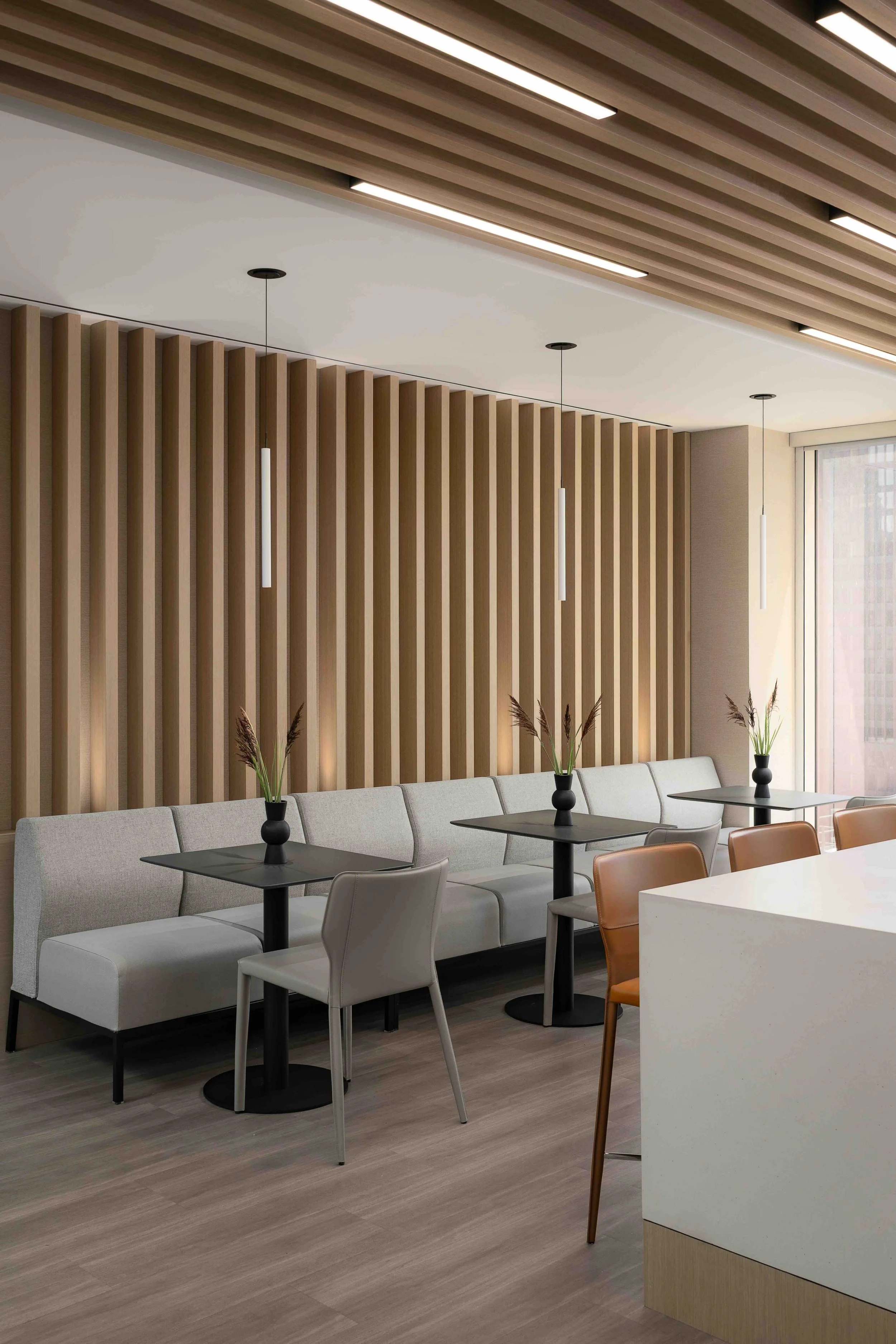 Modern office lounge seating area with wood slat feature wall, café tables, and contemporary workplace design.