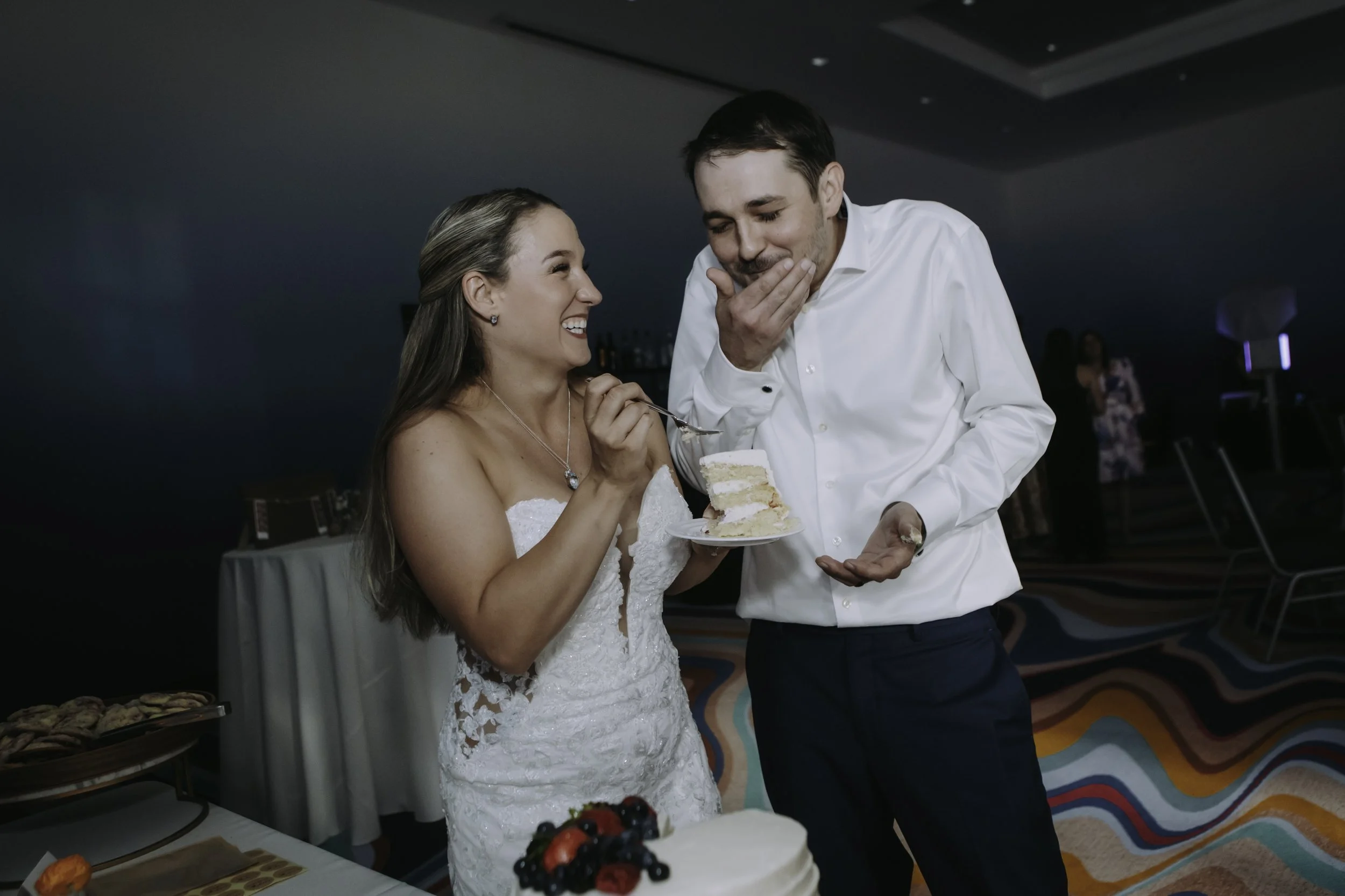 A newlywed couple shares a laugh and a piece of their wedding cake at their reception at The Curtis Hotel in Denver, Colorado.