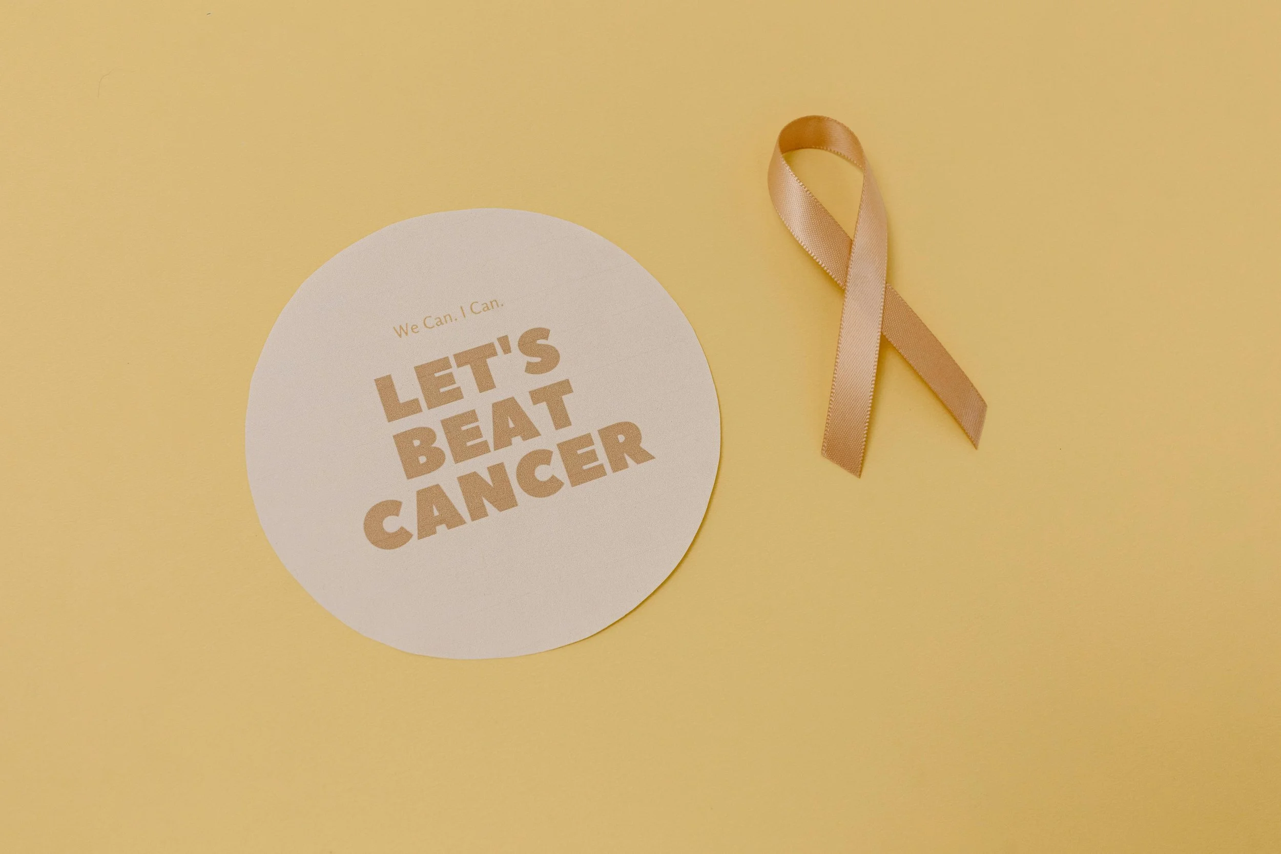 Round "Let's Beat Cancer" card next to a peach awareness ribbon on a yellow background.