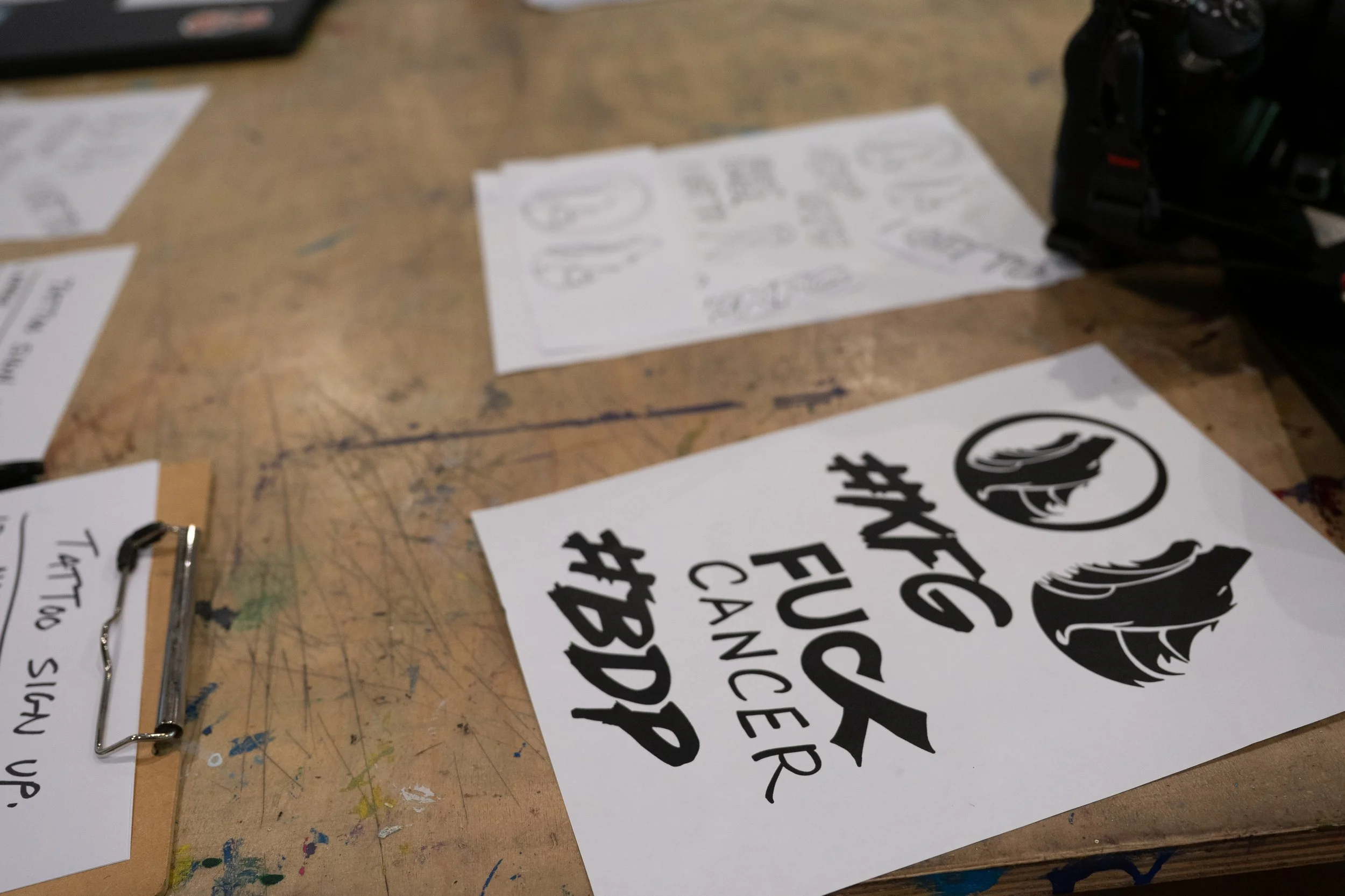 A printed banner with black text and graphic elements lying on a wooden table, partially obscured by other papers and objects.