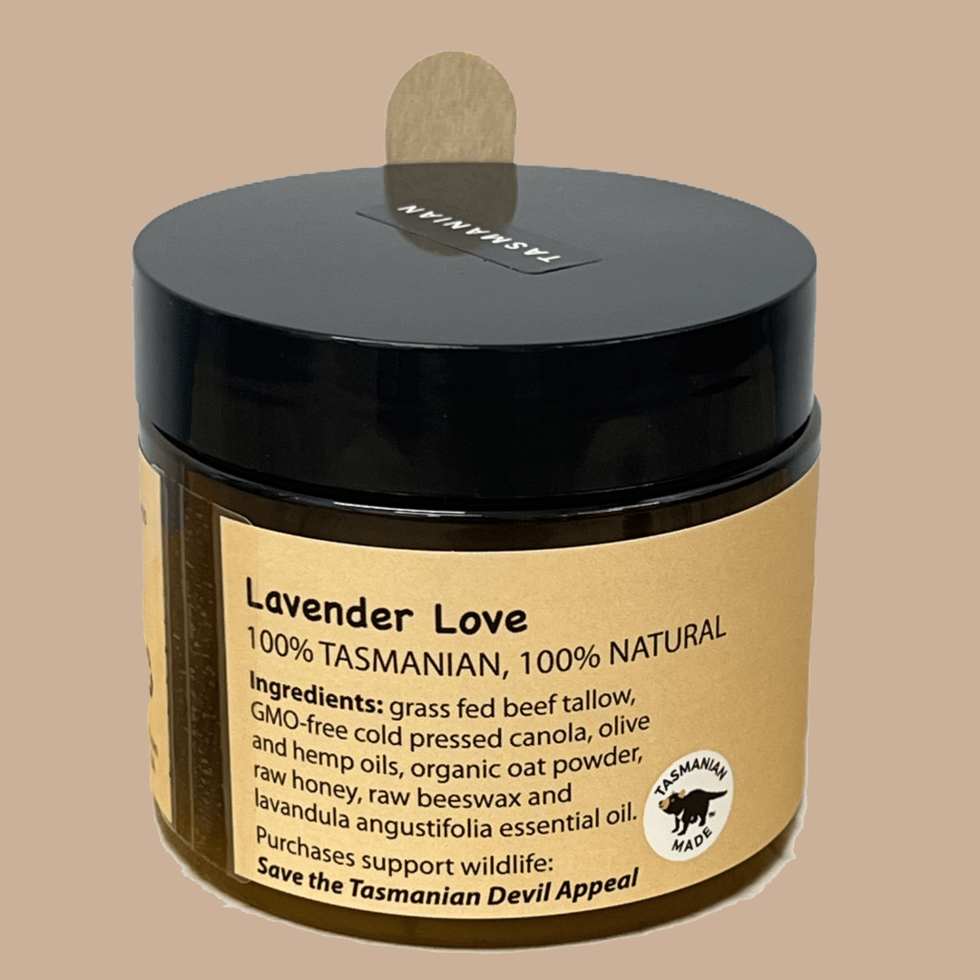 A jar of Lavender Love balm with a black lid and beige label. The label indicates it is 100% Tasmanian and natural, made with ingredients including beef tallow, canola, olive and hemp oils, honey, beeswax, and lavender oil. The jar features a Tasmanian-made logo and encourages supporting wildlife with the slogan 'Save the Tasmanian Devil Appeal'.