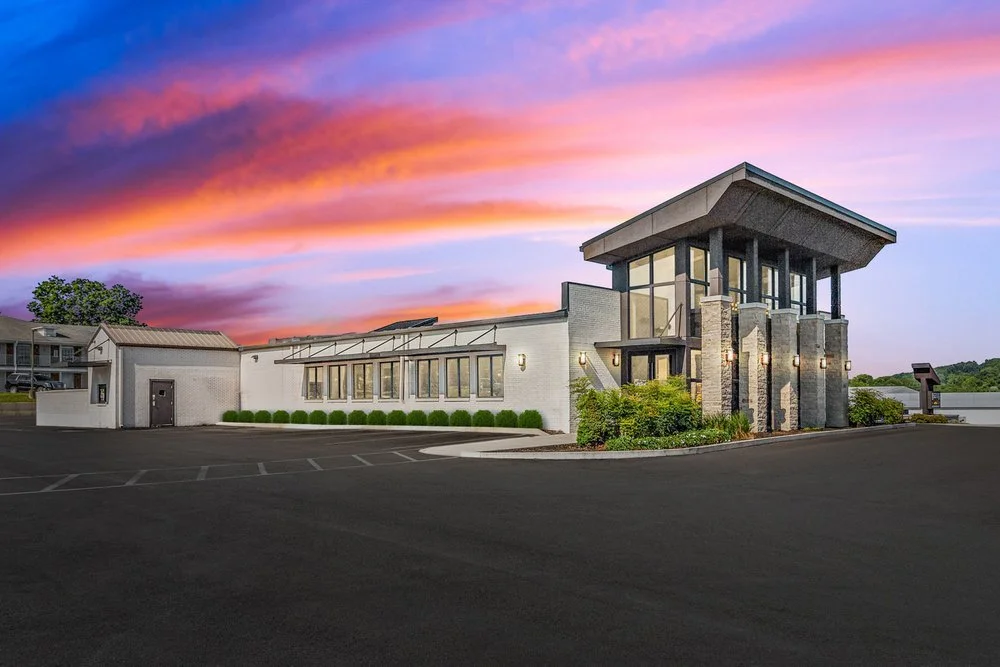 Modern building with large glass windows and stone accents, set against a colorful sunset sky.