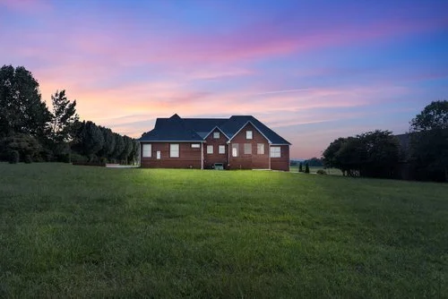 A brick house on a grassy field during sunset with pink and purple sky.