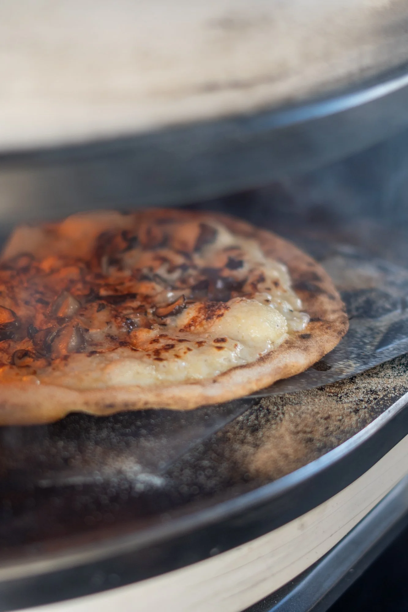 A 'Forest Floor' pizza with toppings of Garlic, Parsley, Shiitake Mushroom, Truffle oil, and Burrata being cooked in a gas pizza oven.