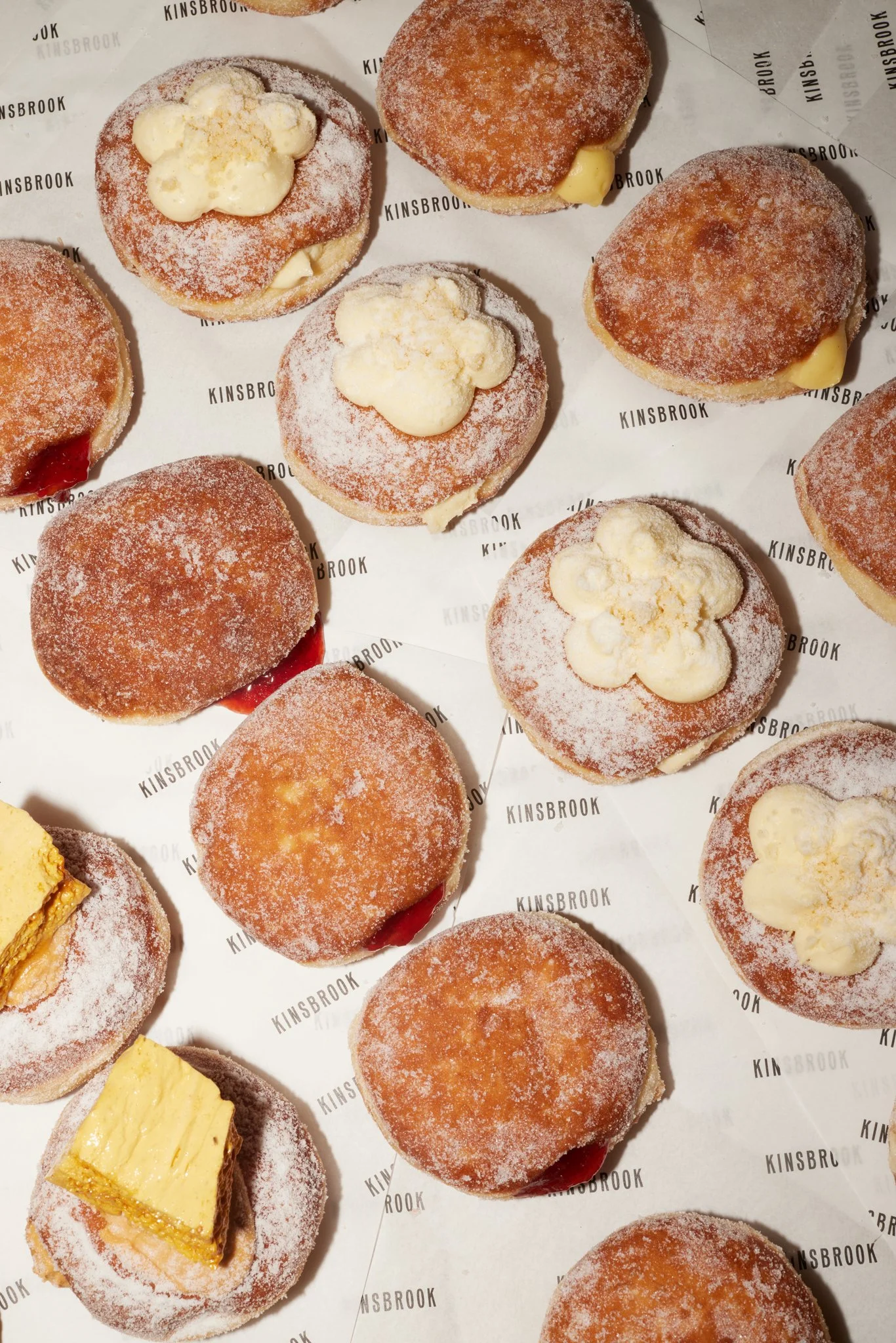 Assorted donuts with various toppings and fillings on Kinsbrook branded paper.