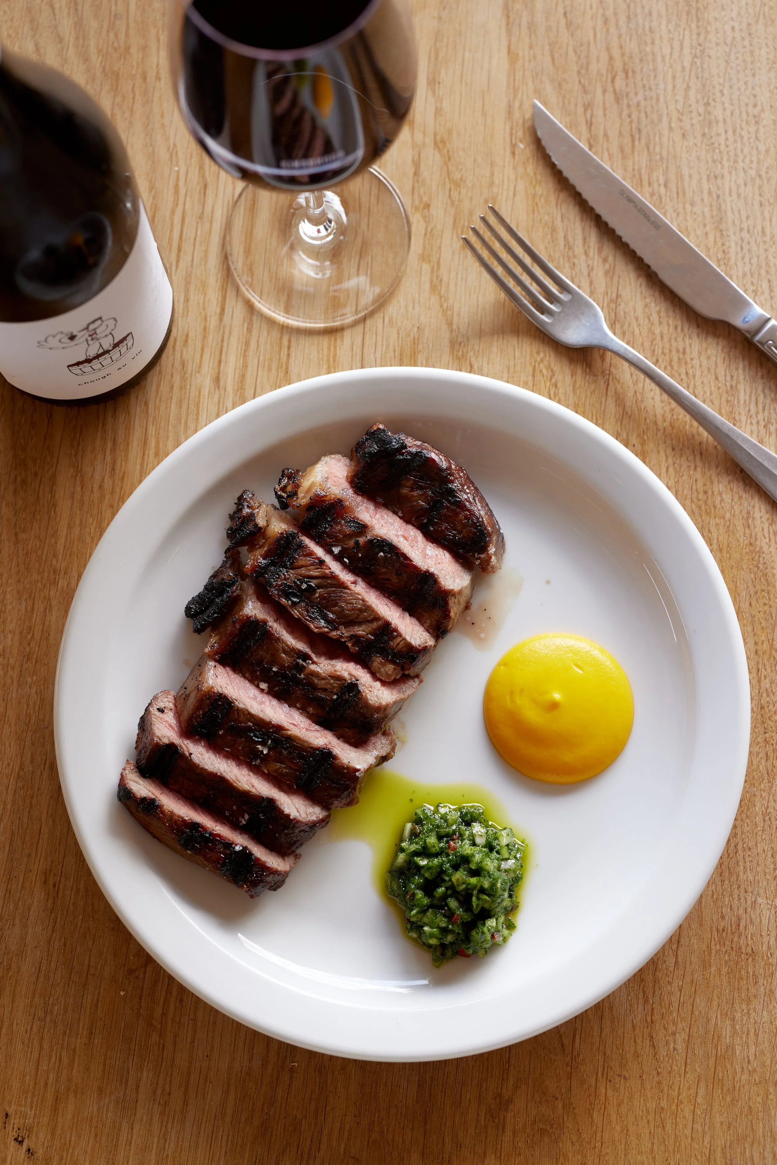 A sliced piece of prime Sussex beef, a glass of Kinsbrook red wine served with chimichurri.