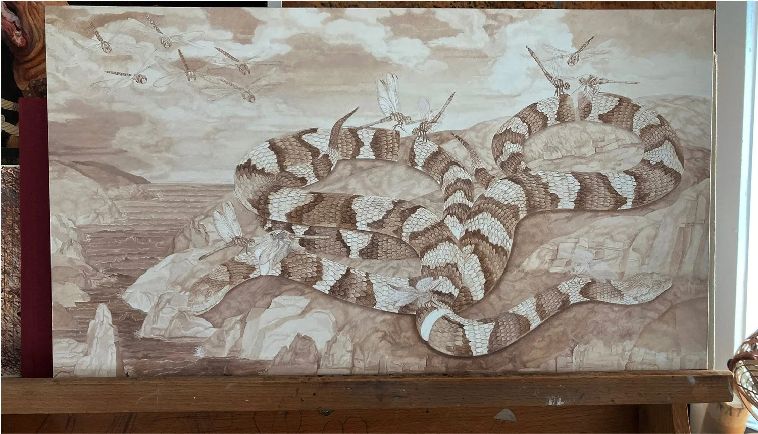 A detailed artwork of a snake entwined with dragonflies in a natural landscape with rocks and mountains.