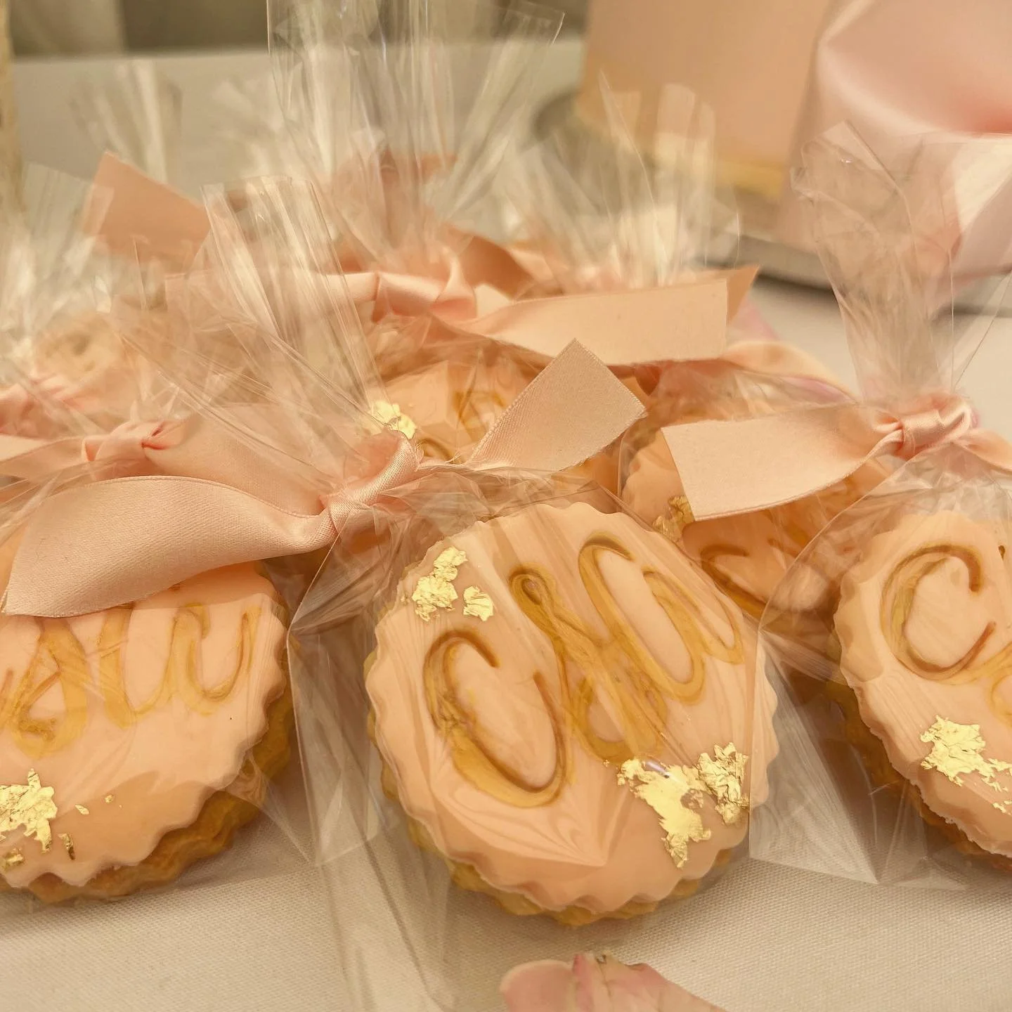 Decorative cookies wrapped in cellophane with gold accents and pink ribbons.