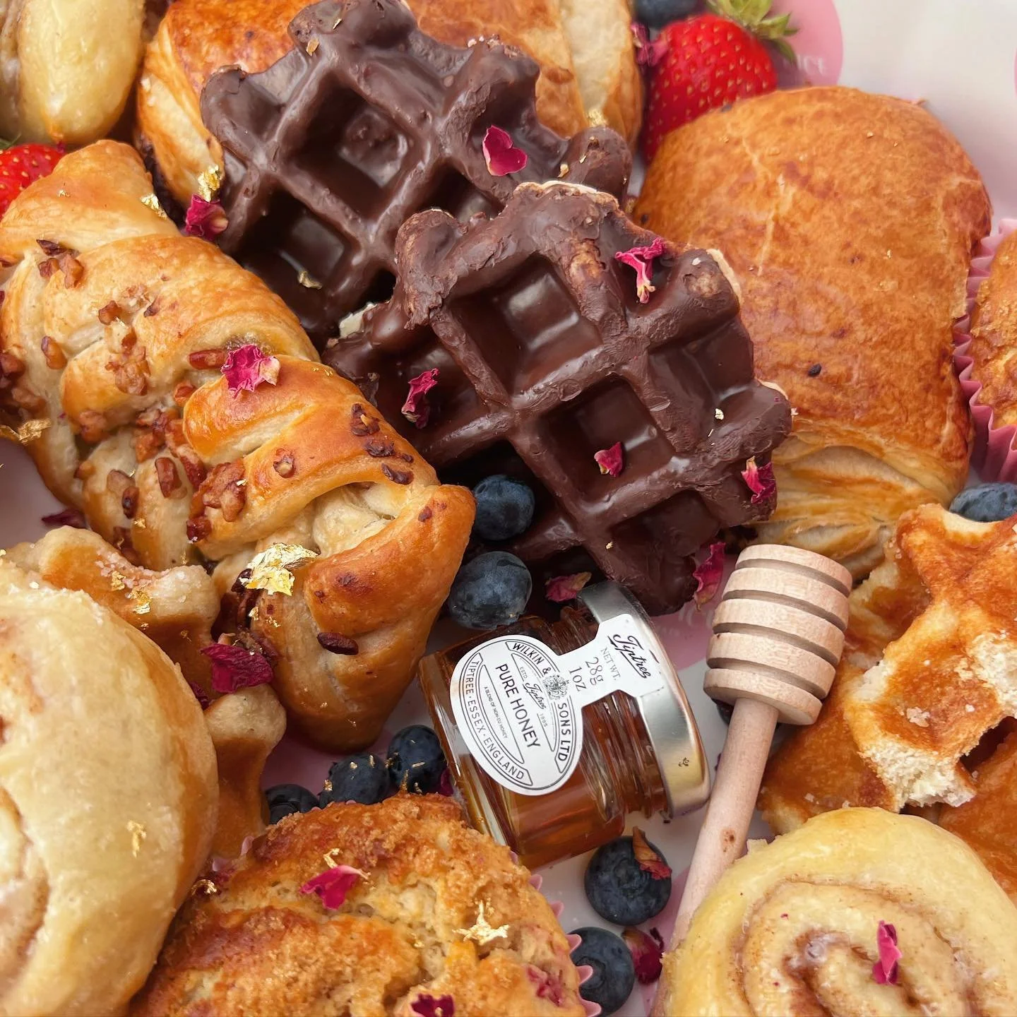 Assorted pastries with chocolate waffles, berries, and honey jar.