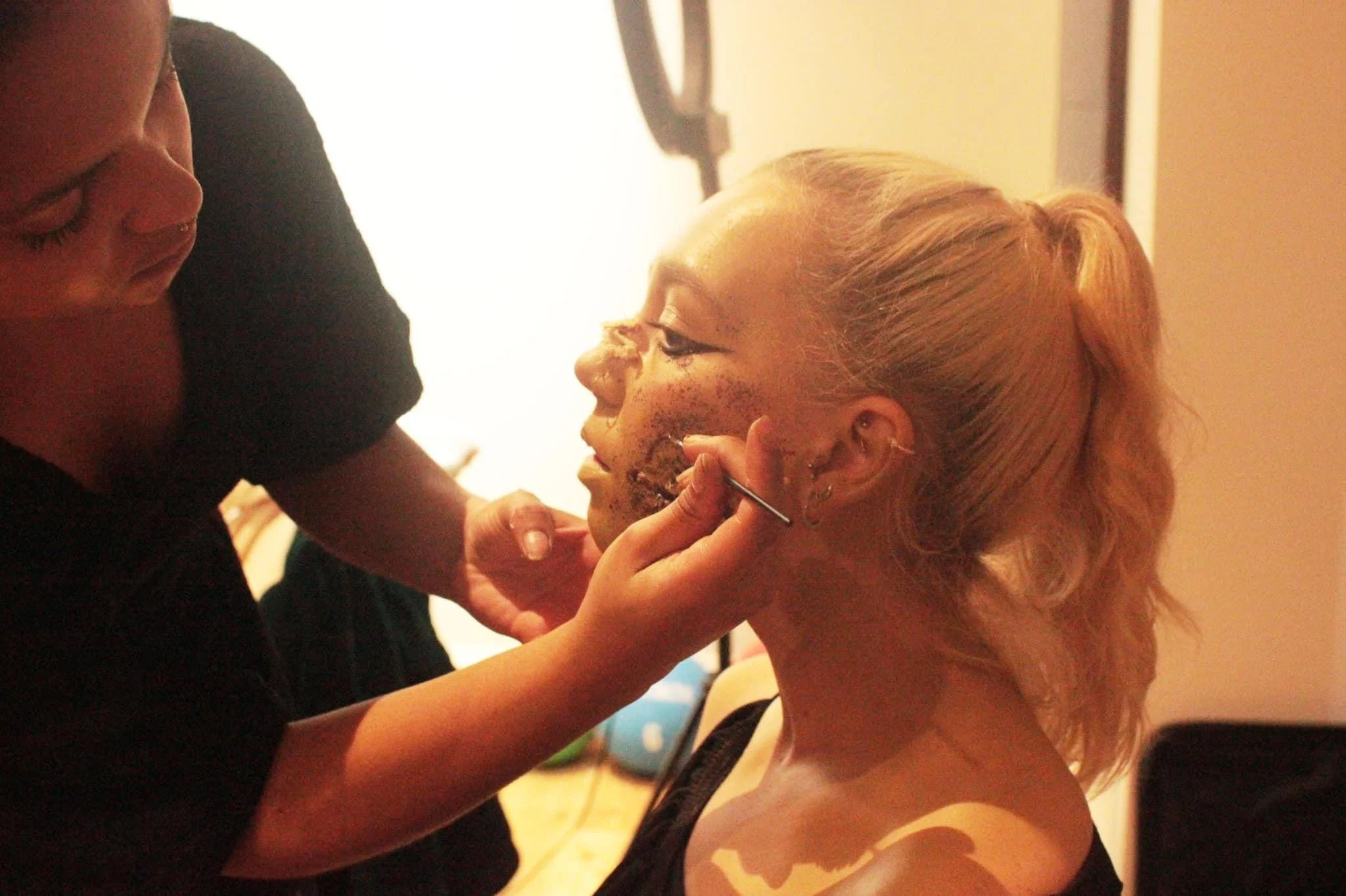 Makeup artist applying makeup to a woman with blonde hair in an indoor setting.