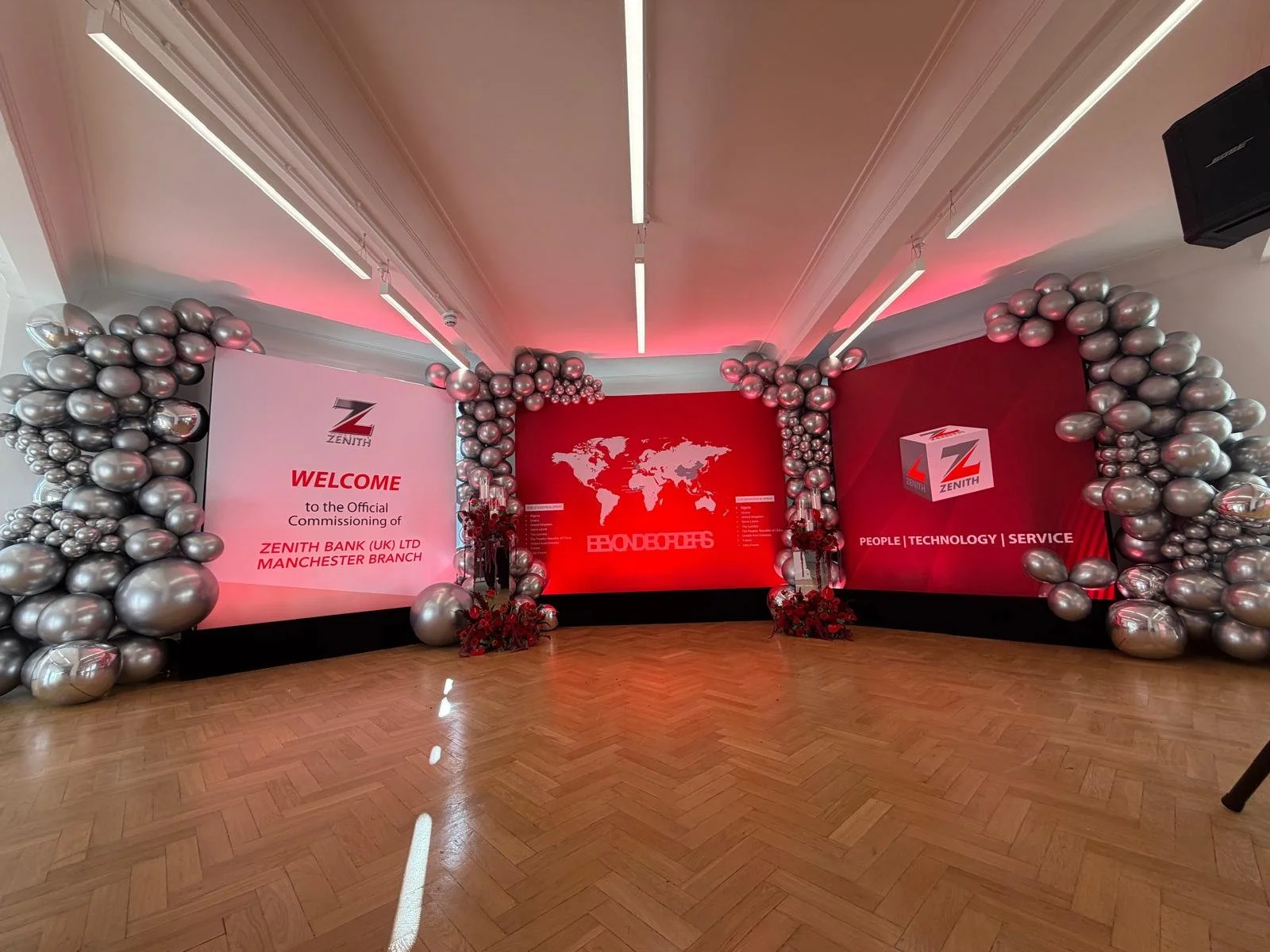 Event space decorated with silver balloons around a large red backdrop displaying the Zenith Bank logo and a world map, with messages about welcoming and technology.