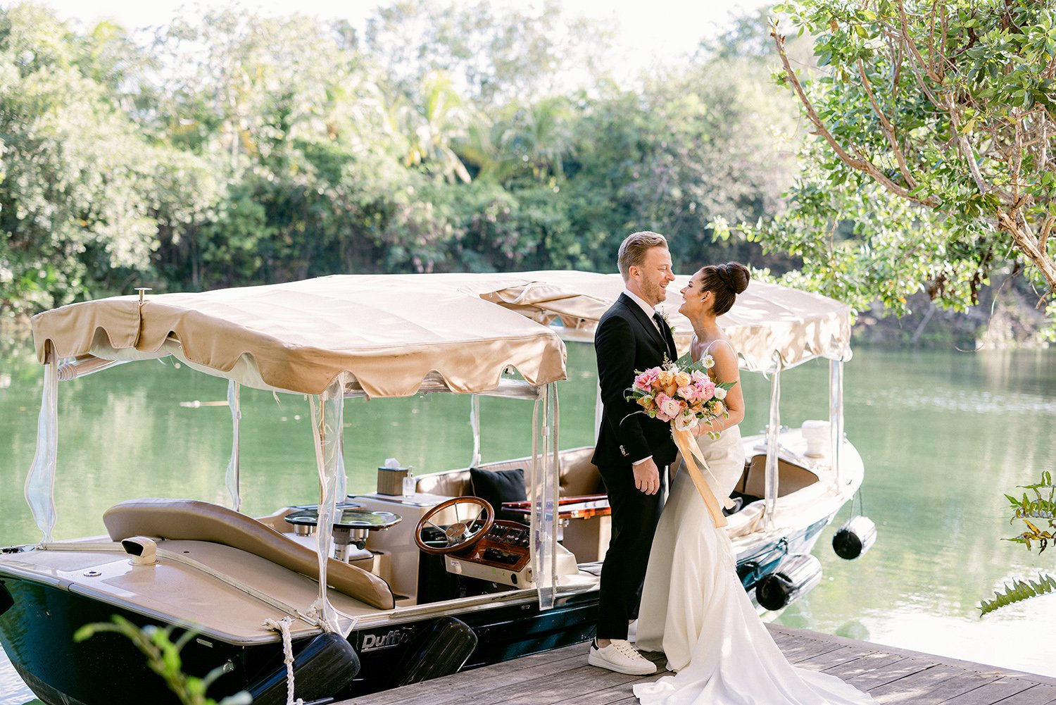 21 lovely photography of bride and groom smiling and looking at each other with a lake and a boat behind surrounded by green tropical plants at Rosewood Mayakoba Riviera Maya Cancun.JPG
