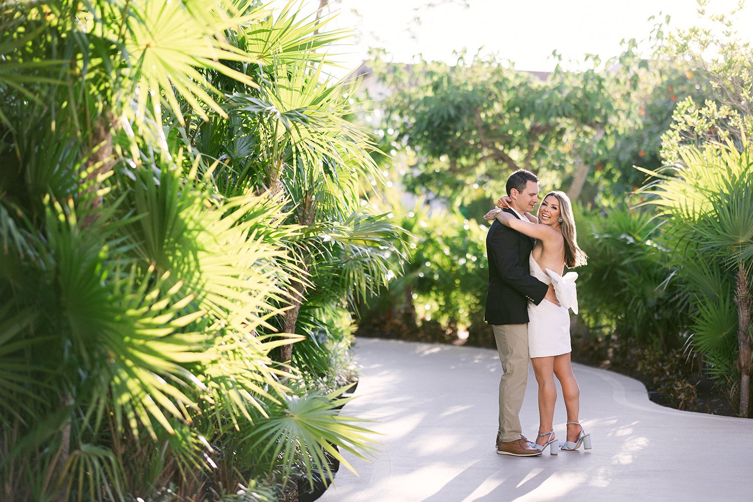03 cute wide photography of smiling bride in white dress hugging groom with palm trees and nature behind at Dreams Riviera Cancun.JPG