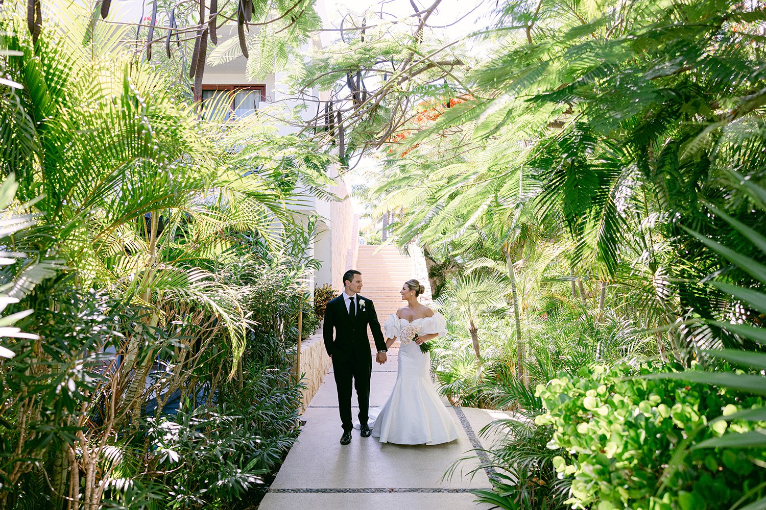 27 cute bride and groom looking at each other holding hands and walking forward with natural green plants aroung them at Dreams Riviera Cancun.JPG