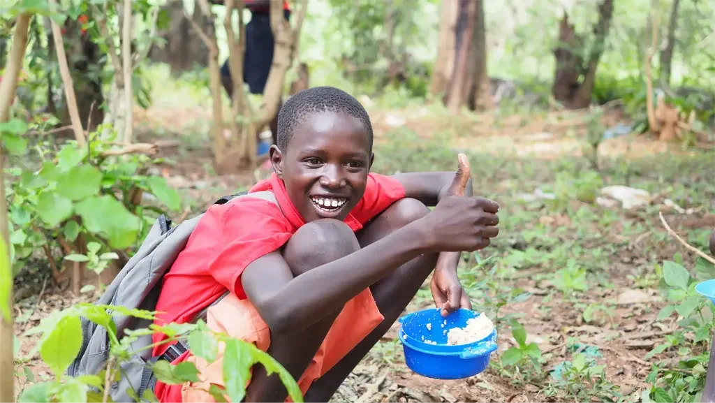 Boy sitting in the forest eating a bowl of food given by Feed the Hungry.