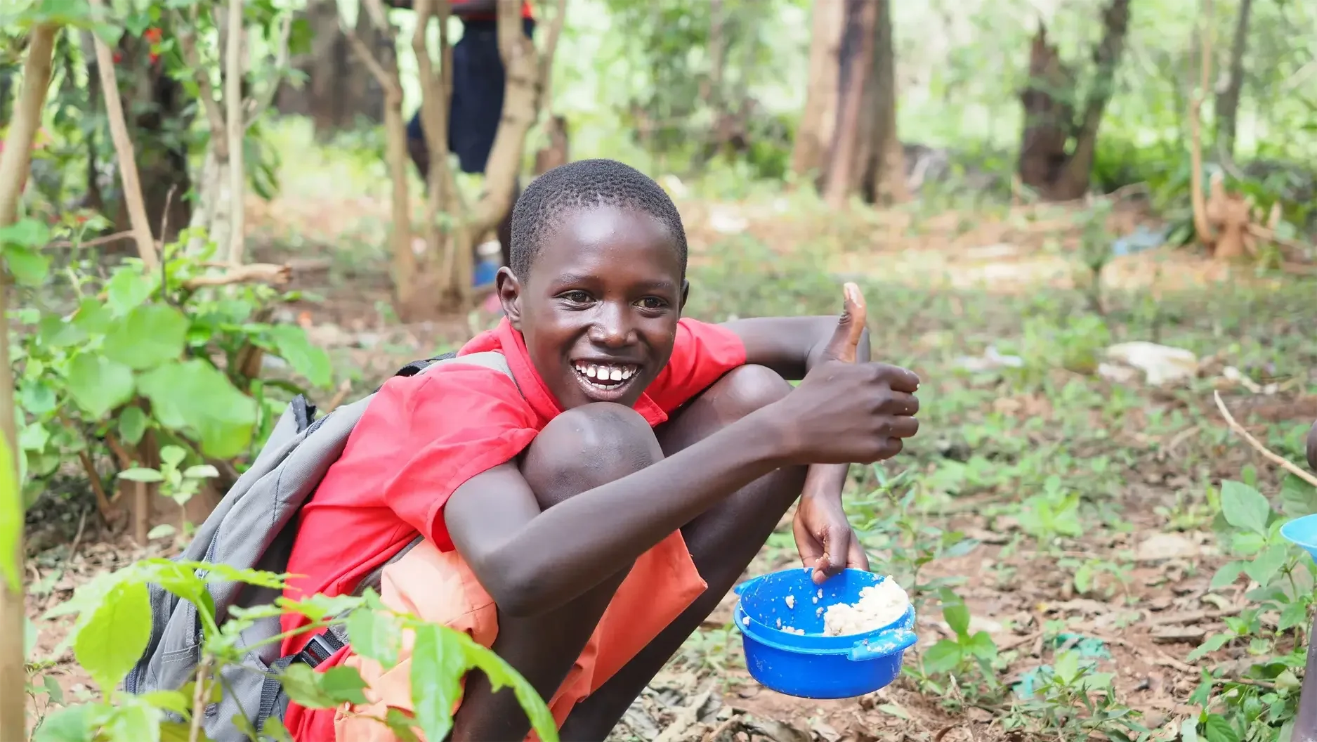 Boy is forest eating a bowl of food provided by Feed the Hungry.
