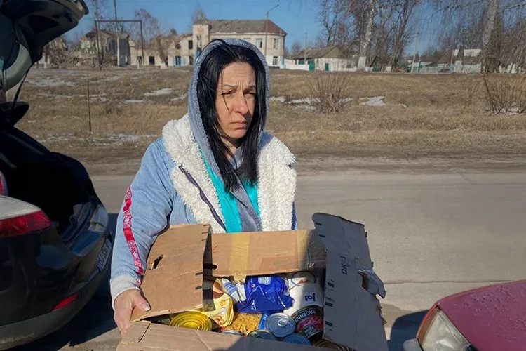A woman with a box of food standing in the road by herself in the cold.