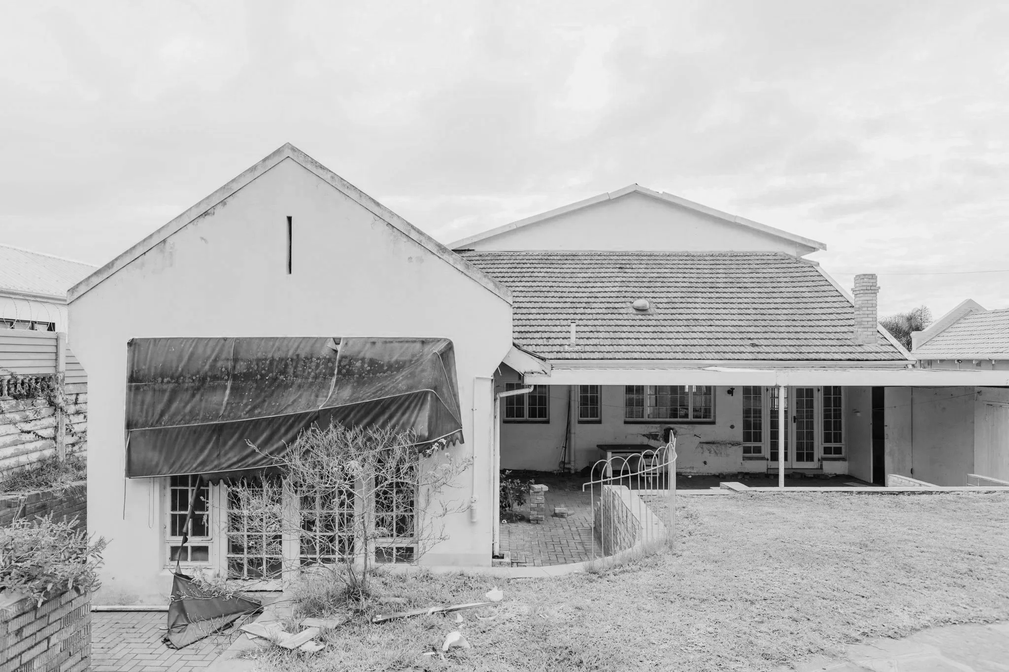 A white house with a red-tiled roof, a small paved patio, and a partially collapsed blue awning.