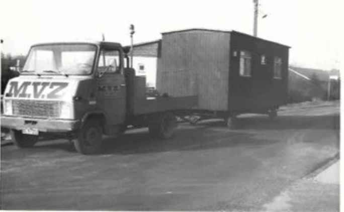 A black and white photo of a military truck with a large wooden structure on its back, parked on a street with no other vehicles or people visible.