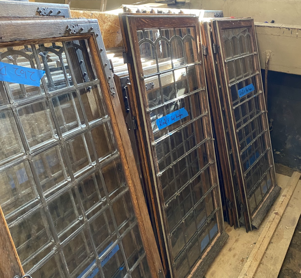 Several vintage wooden and glass window frames stacked against a wall in a workshop or storage area.