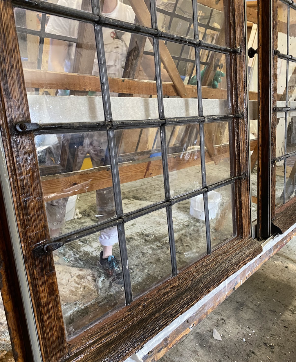 Wood-framed windows with multiple small glass panes in a workshop, reflecting interior construction activities.