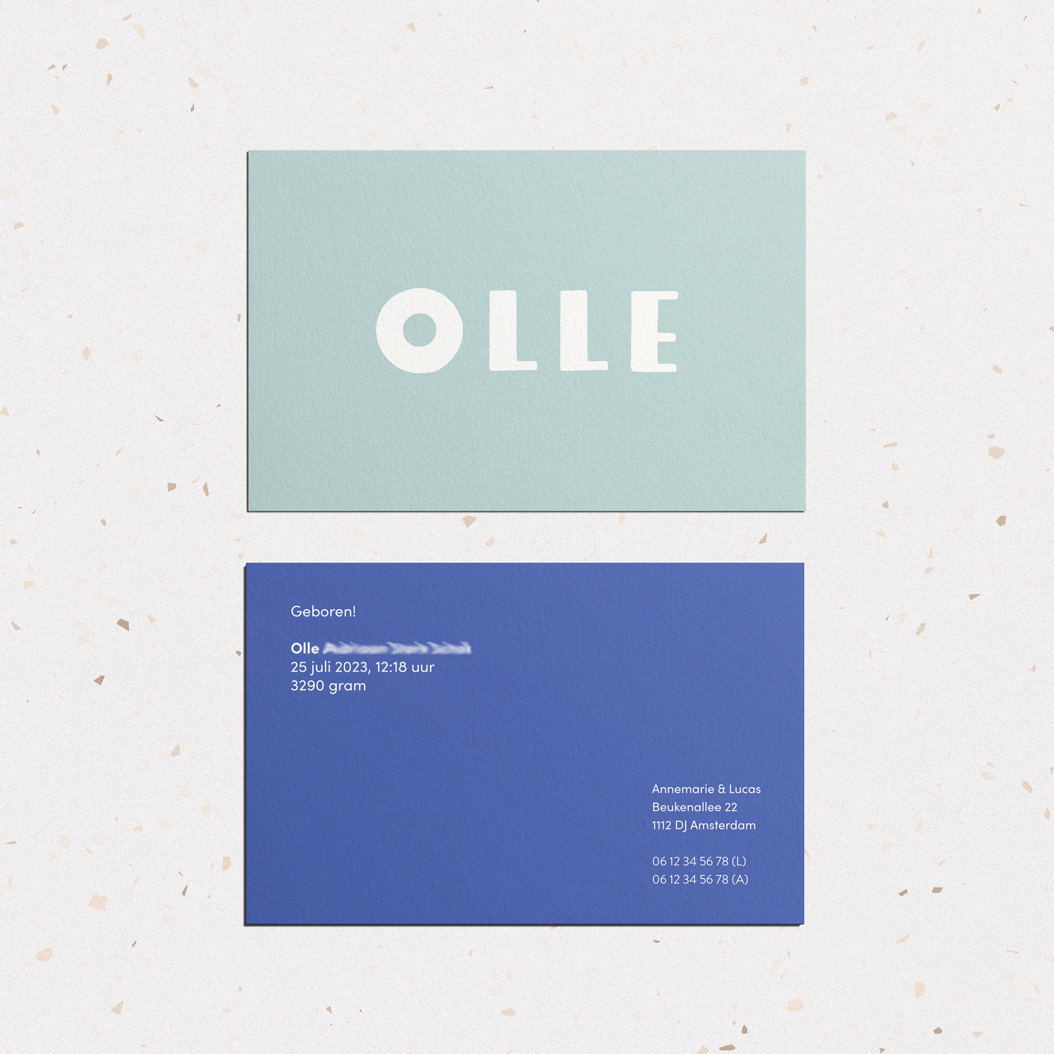 Foto waarbij het ontwerp van een geboortekaartje getoond wordt in lichtblauw, met hoofdletters de naam van het kindje: 'Olle' in het wit erop gedrukt. 