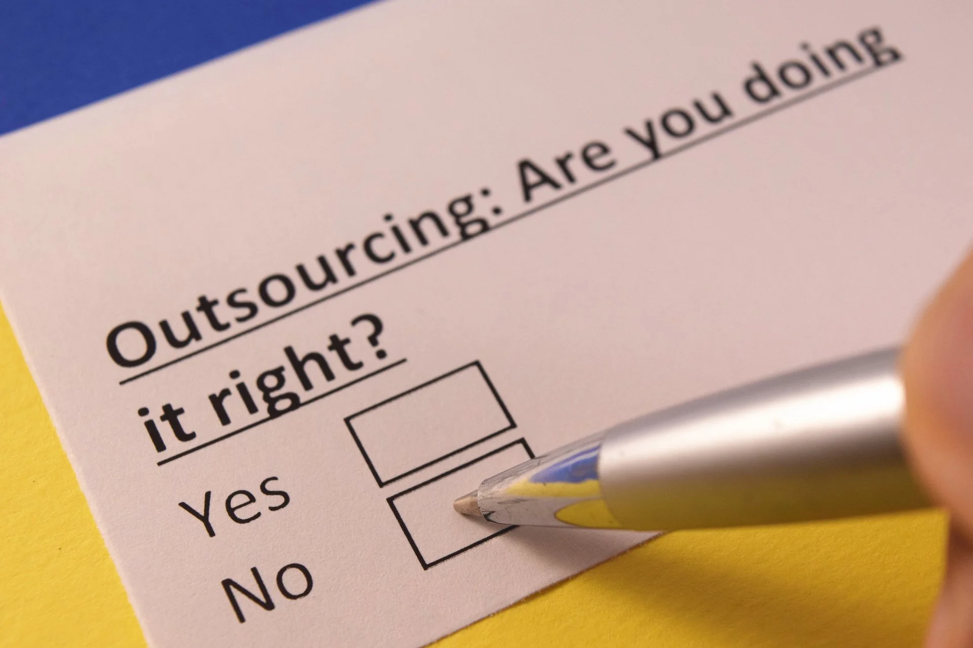 Close-up of a survey or questionnaire asking, "Outsourcing: Are you doing it right?" with options for Yes and No and a person marking the Yes box with a silver pen.