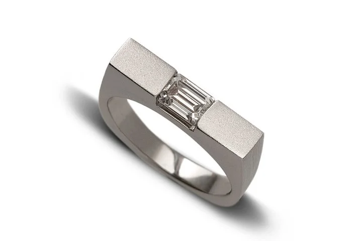 Very contemporary linear ring with emerald cut diamond.  This is customizable with other stones and finishes.  Here in white gold with diamond and a matte/sandblast finish.  This works great as an engagement ring or a stackable.

#engagmentring #stac