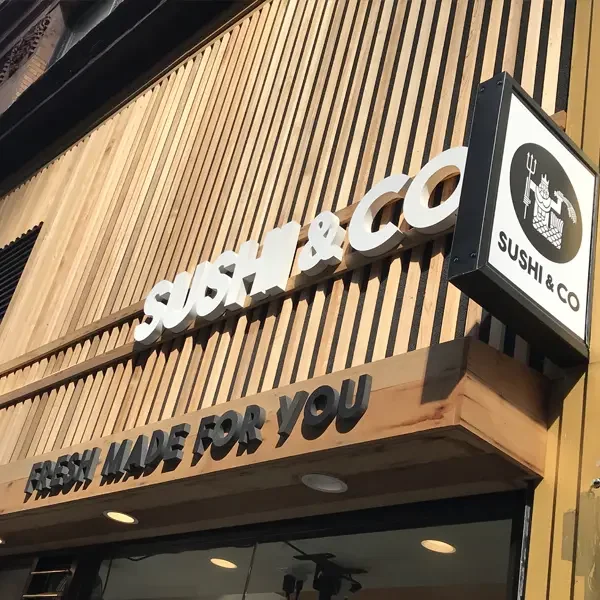 Sign of Sushi & Co restaurant with a wooden exterior, large white text reading "SUSHI & CO," a smaller text sign saying "FRESH MADE FOR YOU," and a sushi logo on a black and white square sign.
