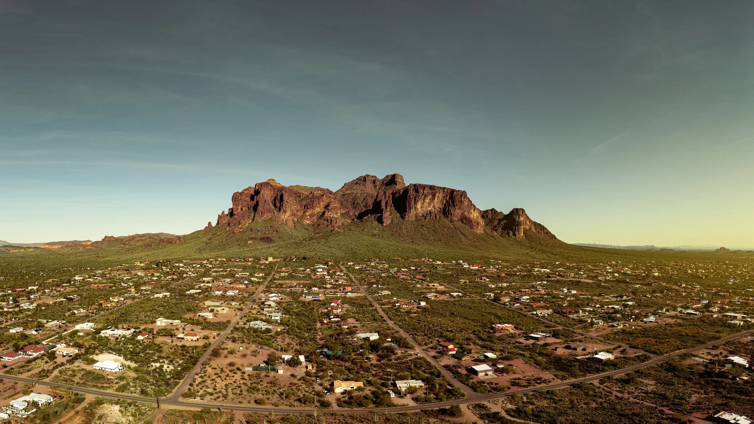 A mountain overlooking a suburban area with houses, roads, and desert vegetation in the foreground.