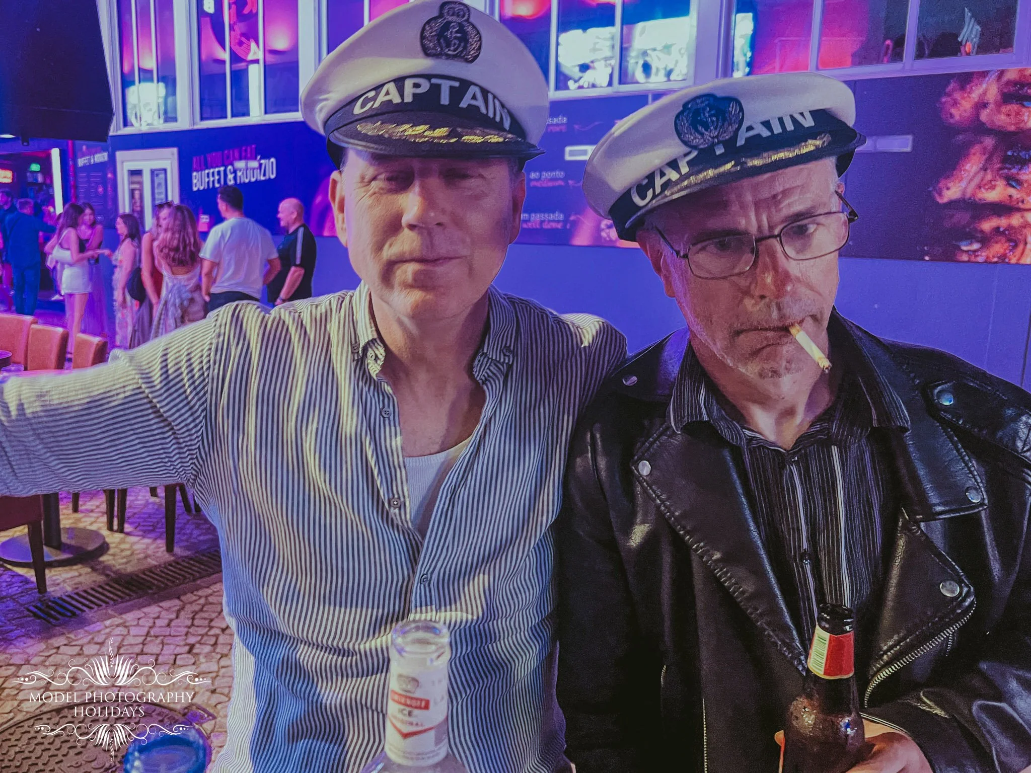 Two men wearing captain hats at a nightlife venue with purple neon lights, other people, and a visible sign for a buffet and studio in the background.