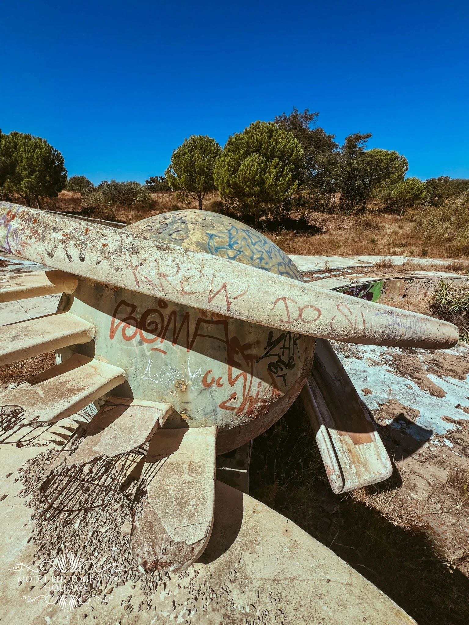 An abandoned boat covered in graffiti sitting on dry land with trees and blue sky in the background.