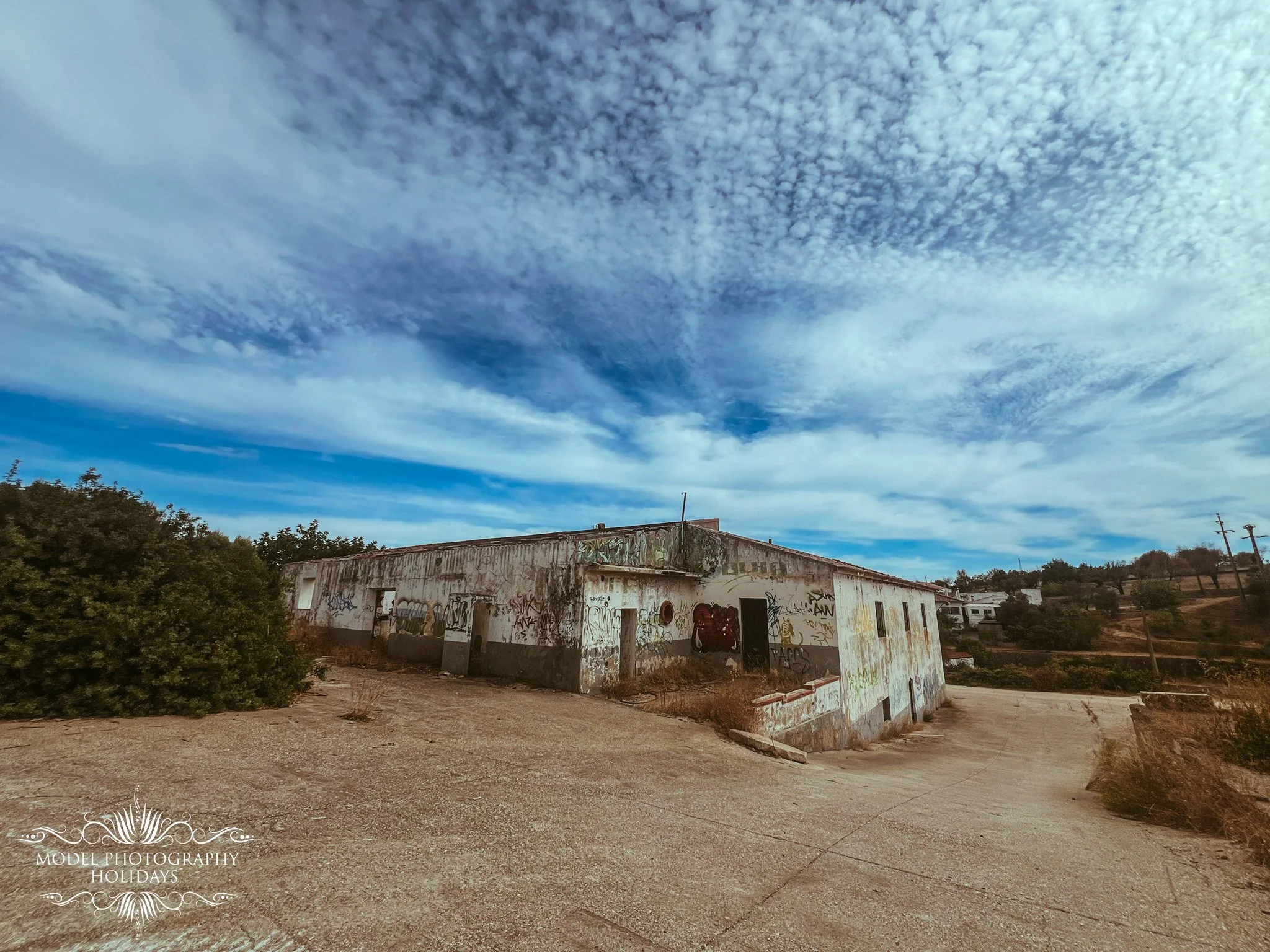 An abandoned building covered in graffiti with a cloudy sky overhead and trees in the background.
