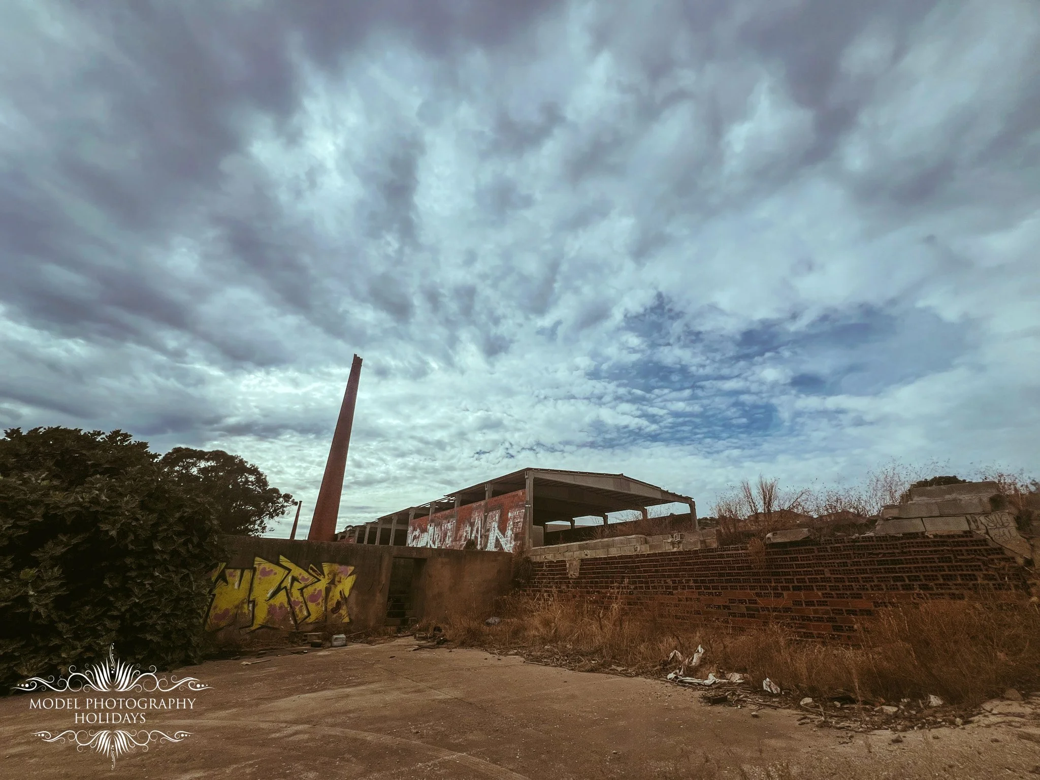 A cloudy sky over an urban area with graffiti-covered walls, trees, and an unfinished building with graffiti on its walls.