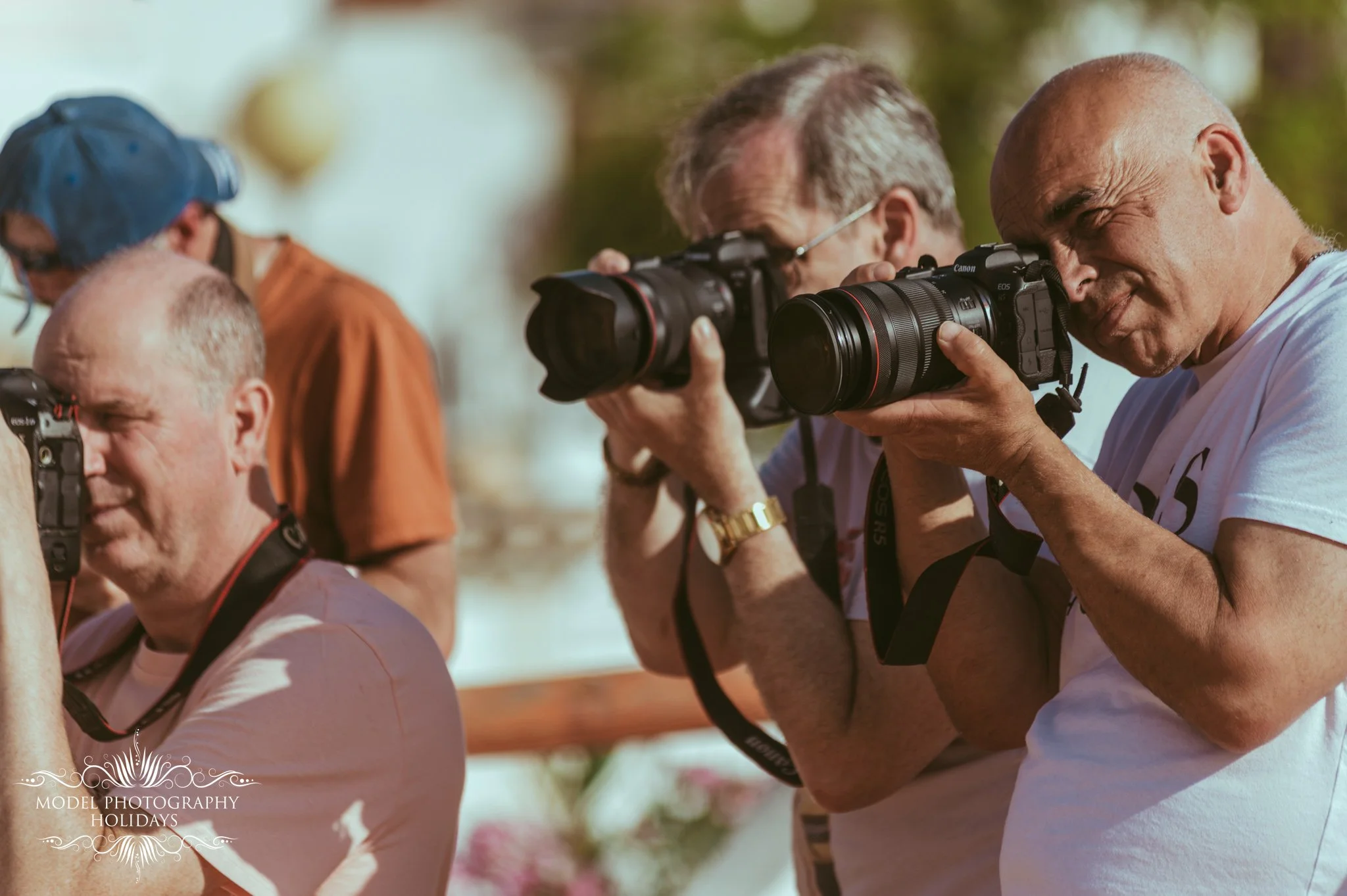 Three men taking photographs outdoors, two with professional cameras and one with a smaller camera, during daytime.