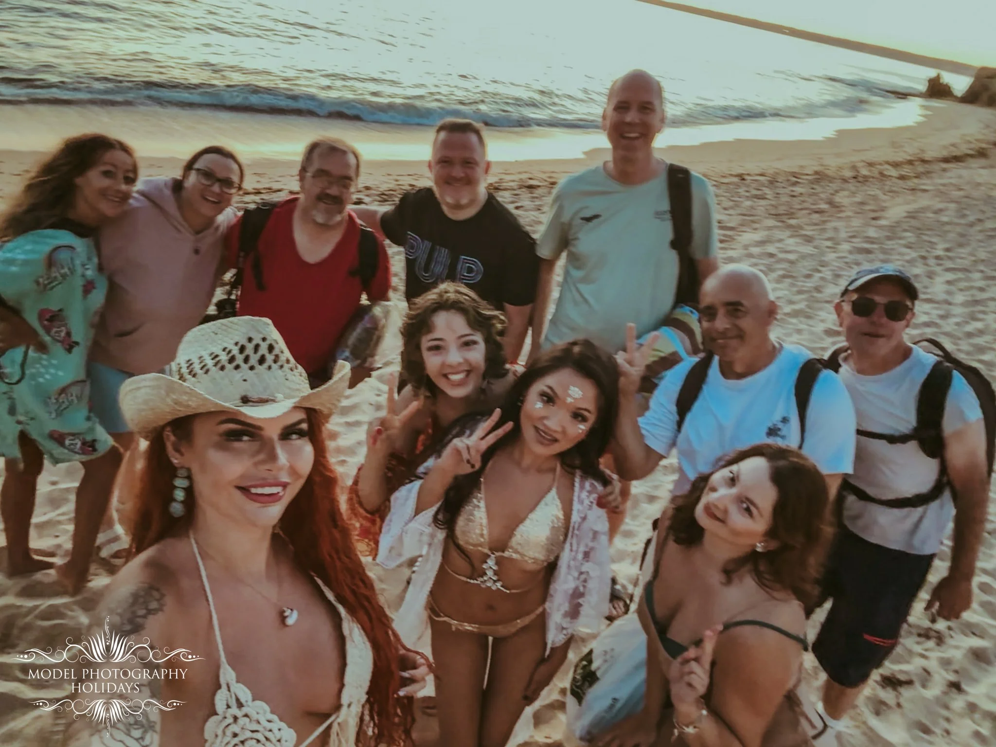 Group of people smiling and posing for a photo on the beach at sunset