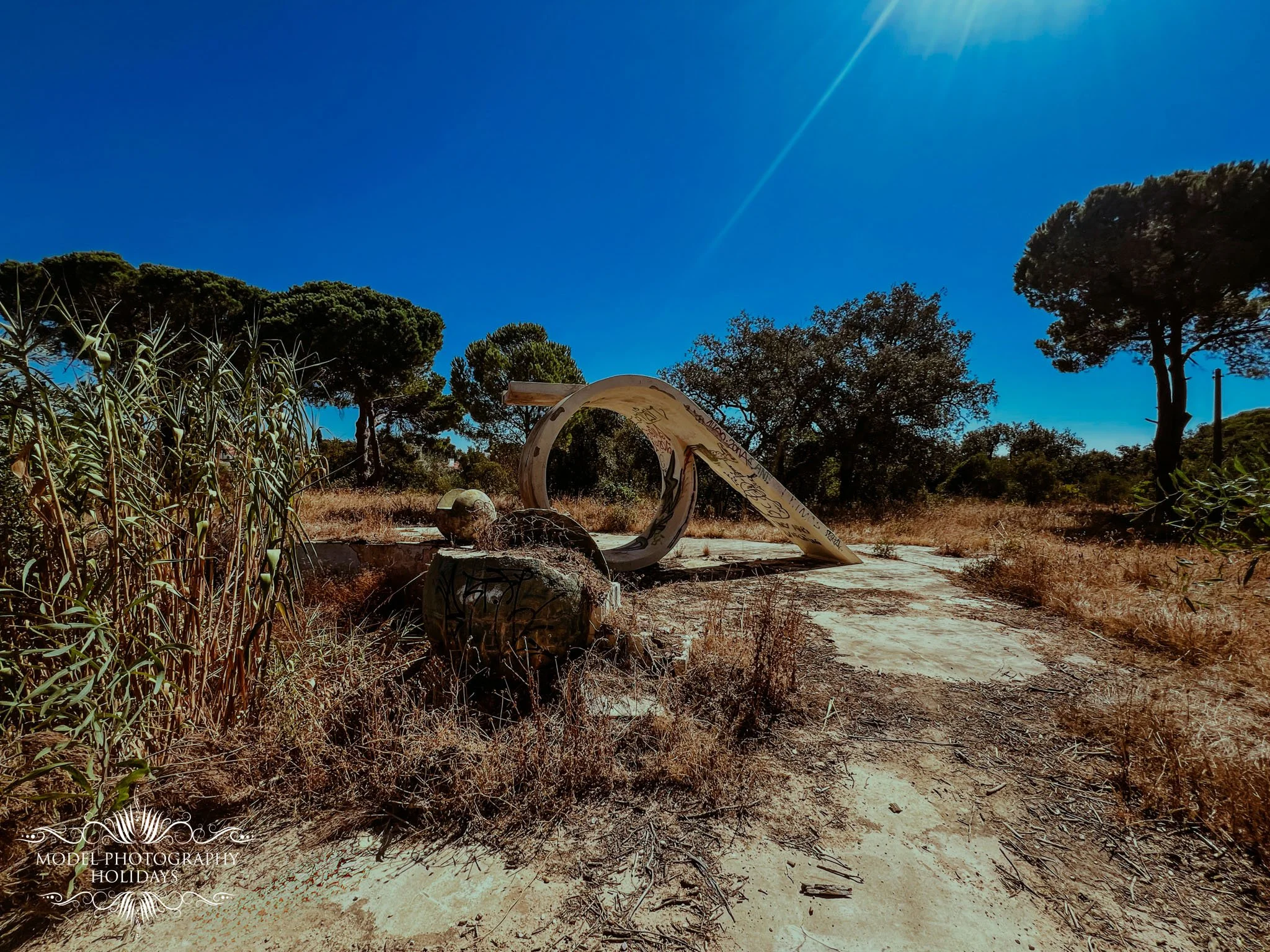 Abandoned soap sculpture on dry ground surrounded by trees and bushes under a sunny blue sky.