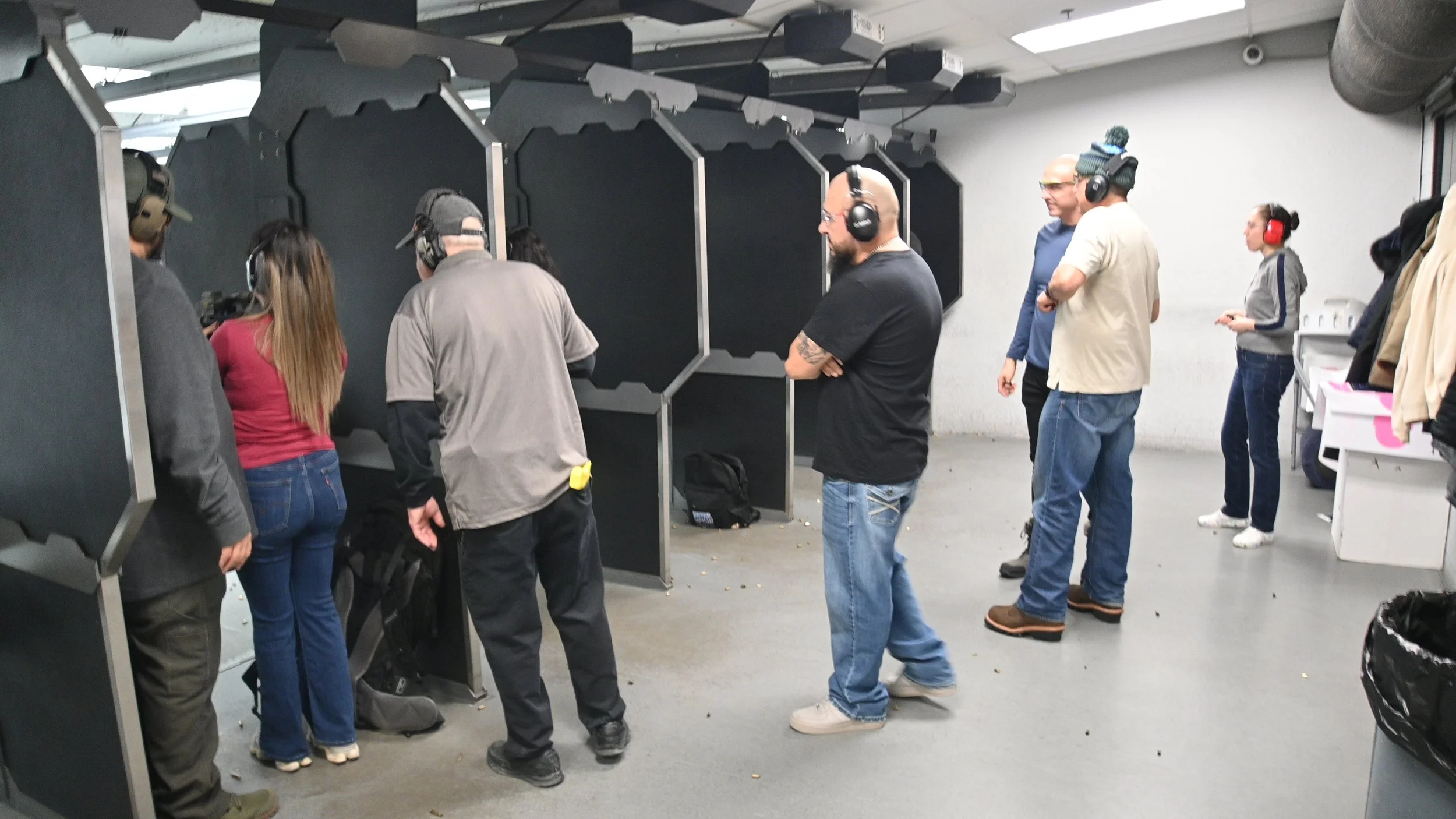 People wearing headphones standing in line at an indoor shooting range.
